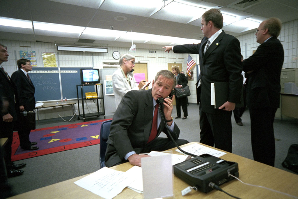 As Deputy Assistant Dan Bartlett points to news footage of the World Trade Center, President George W. Bush gathers information about the attack from a classroom at Emma E. Booker Elementary School in Sarasota, Fla. on Sept. 11, 2001.