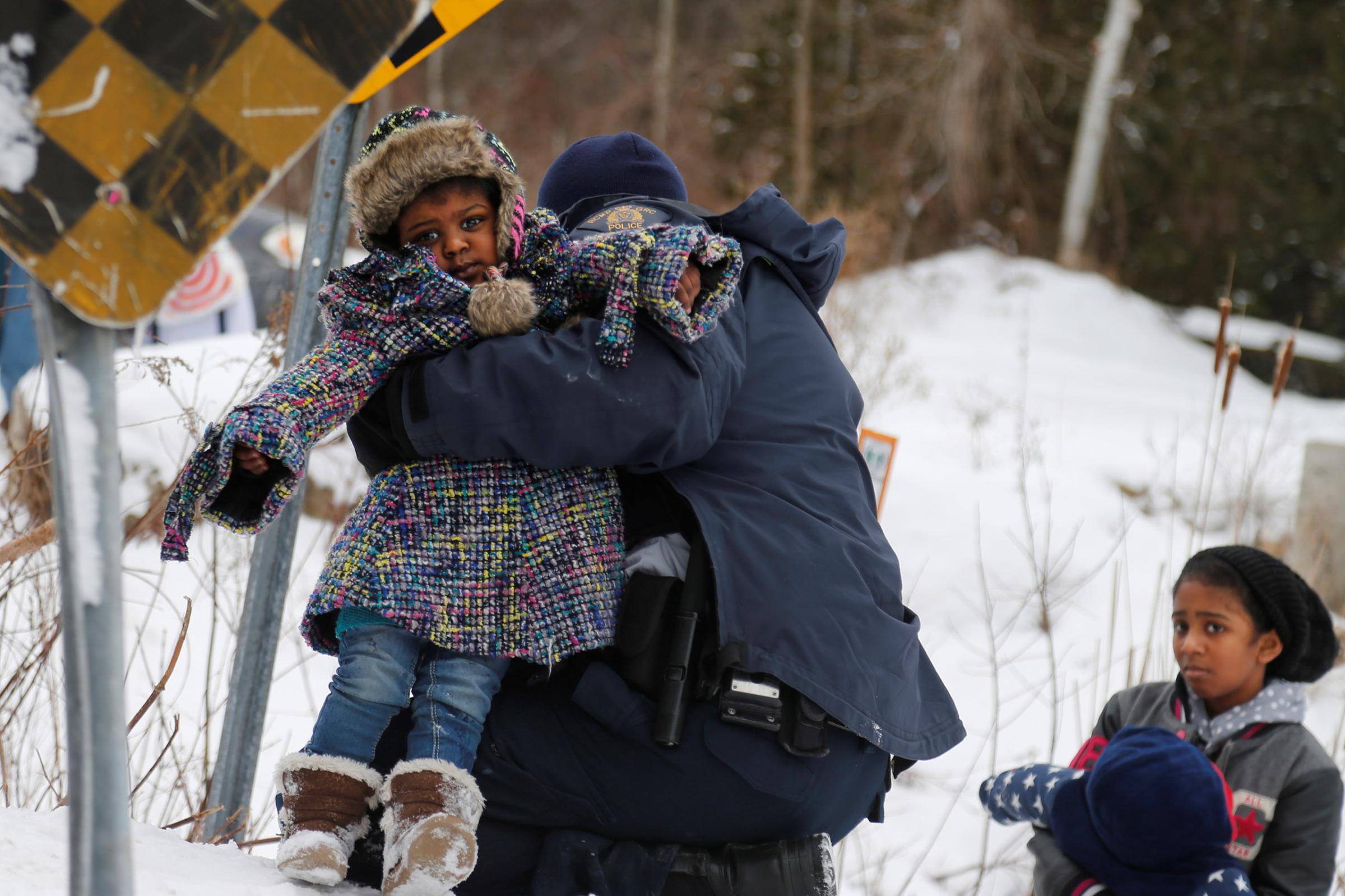 A child is helped up a hill by Royal Canadian Mounted Police officers after a family arriving by taxi and claiming to be from Sudan are taken into custody after walking across the U.S.-Canada border into Hemmingford, Quebec