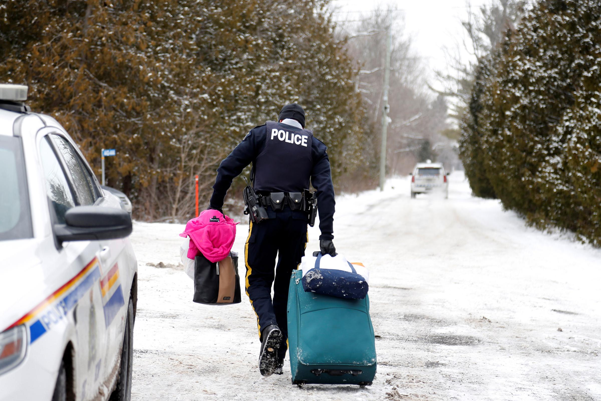 A Royal Canadian Mounted Police officer carries luggage of a woman and her family who told police they were from Sudan and were taken into custody after arriving by taxi and walking across the U.S.-Canada border into Hemmingford, Quebec