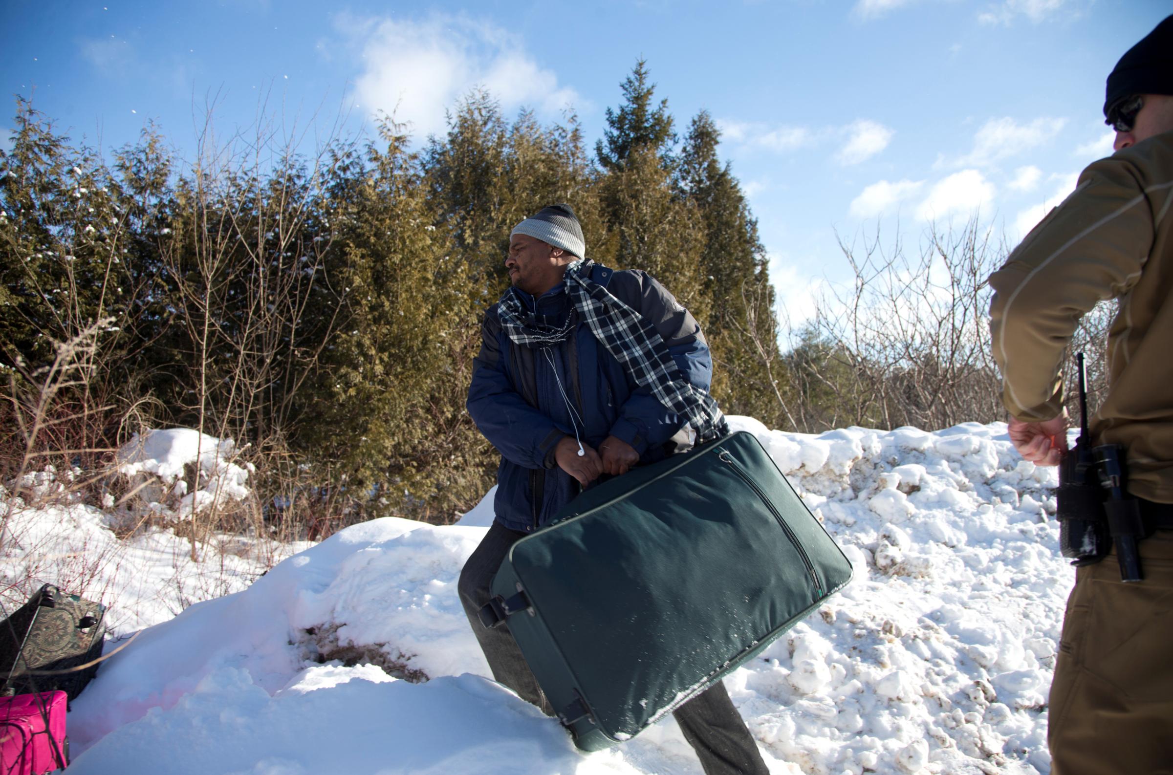 A man who claimed to be from Sudan throws his family's suitcases towards the border as he is detained by a U.S. border patrol officer after his family crossed the U.S.-Canada border into Hemmingford, Canada, from Champlain in New York, U.S., February 17, 2017. REUTERS/Christinne Muschi - RTSZ6NV