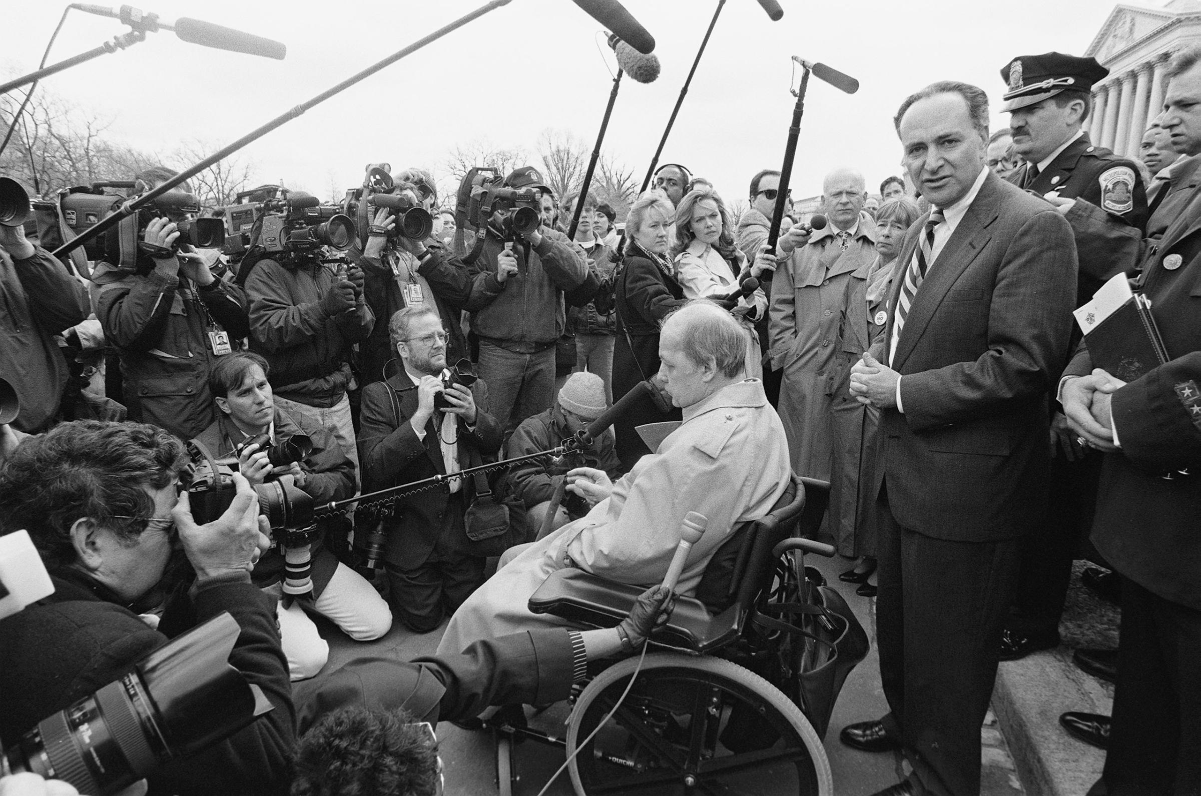 Schumer, stands behind Jim Brady, who was shot in the head during John Hinckley's assassination attempt on President Ronald Reagan, during a news conference outside the the U.S. Capitol supporting the assault weapons ban, March, 22, 1996.