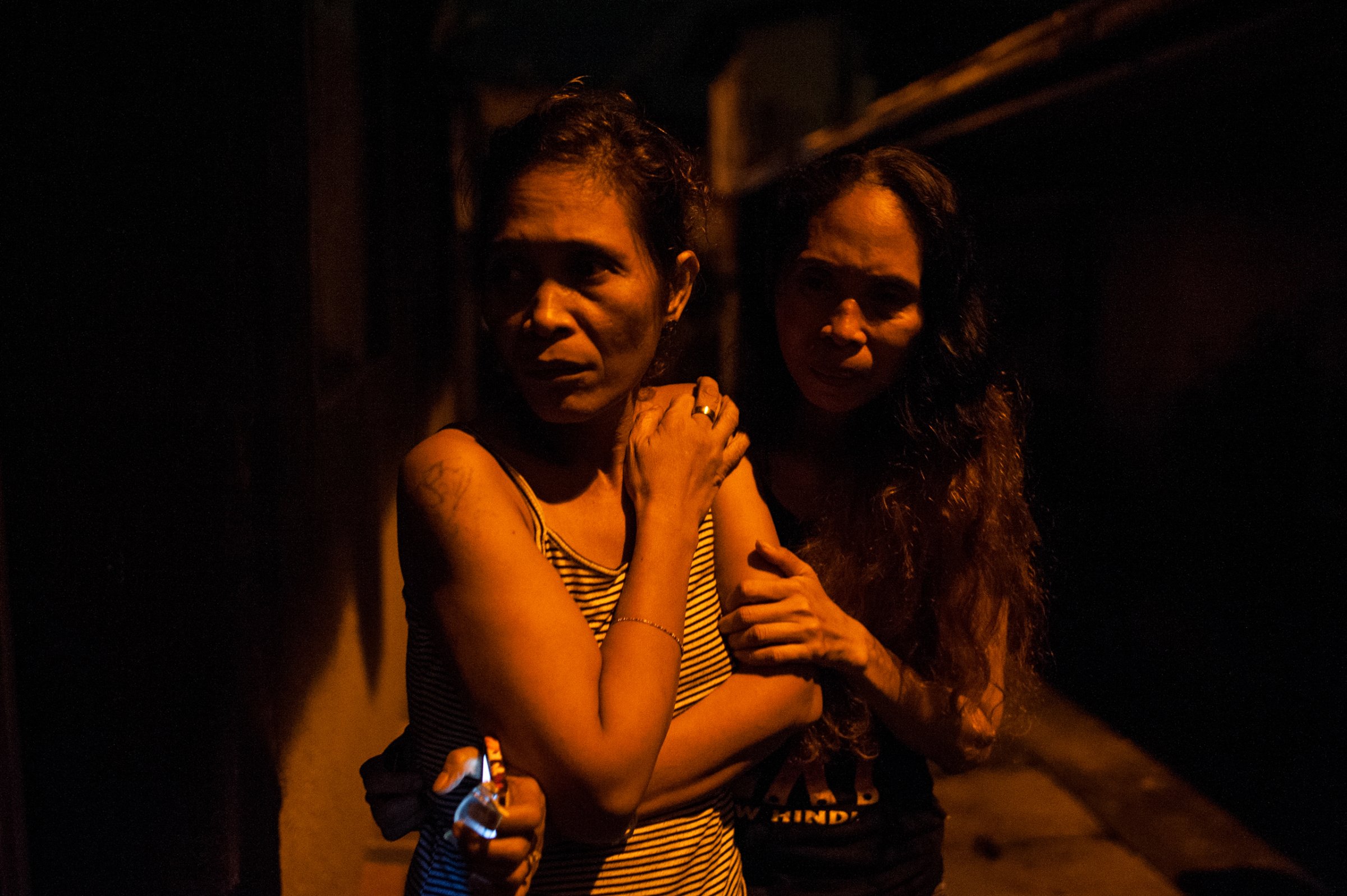 Two women watch as the body of their kin is examined by police after masked assailants barged into their home and dragged him into the streets and shot him in Manila in September 2016.