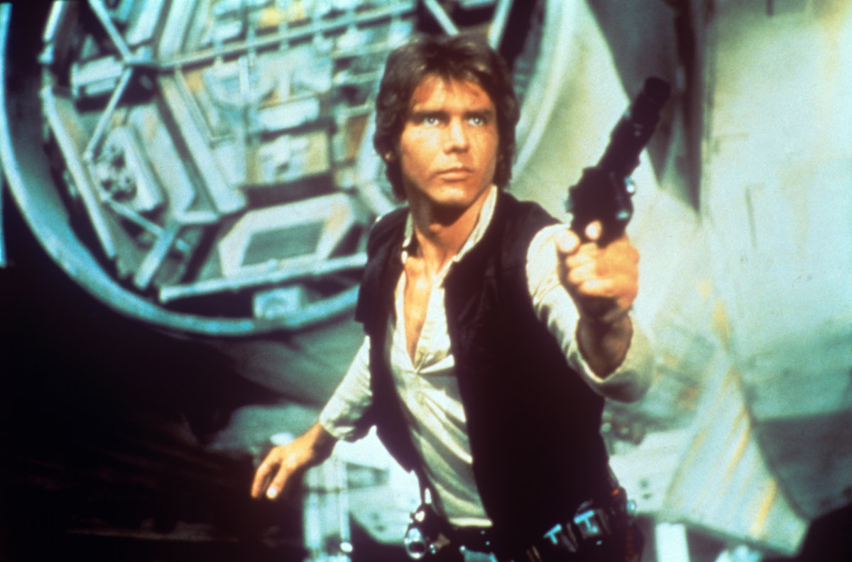 In a scene from George Lucas' epic space opera Star Wars, the American actor Harrison Ford as rebel smuggler Han Solo draws a gun against enemies; behind him can be seen a fantastic space shuttle. USA, 1977. (Mondadori Portfolio / Getty Images)
