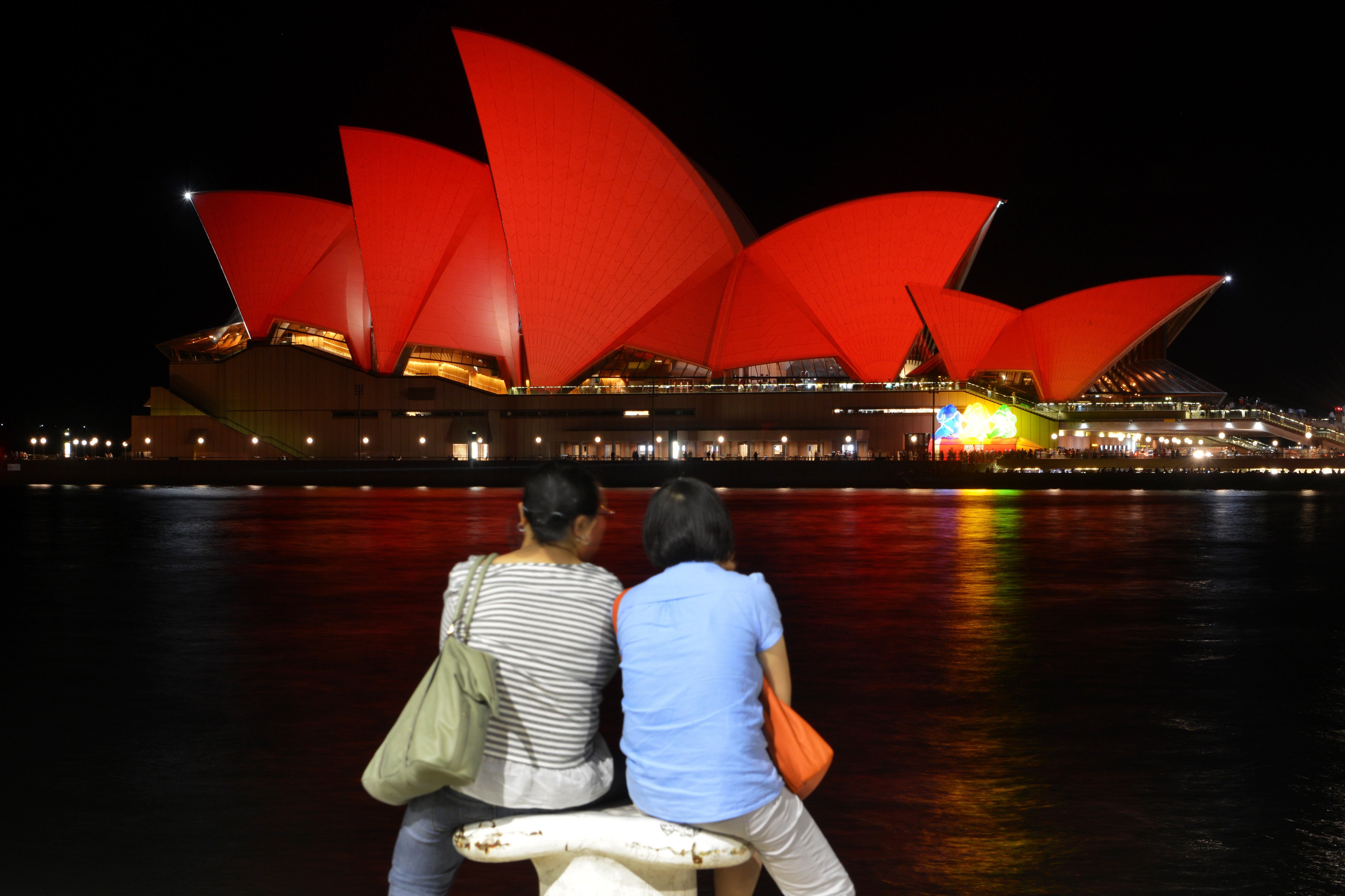 Chinese tourists sit and view the Sydney Opera House, which is lit up in red to welcome in the Lunar New Year, in Sydney on Feb. 8, 2016 (Peter Parks—AFP/Getty Images)
