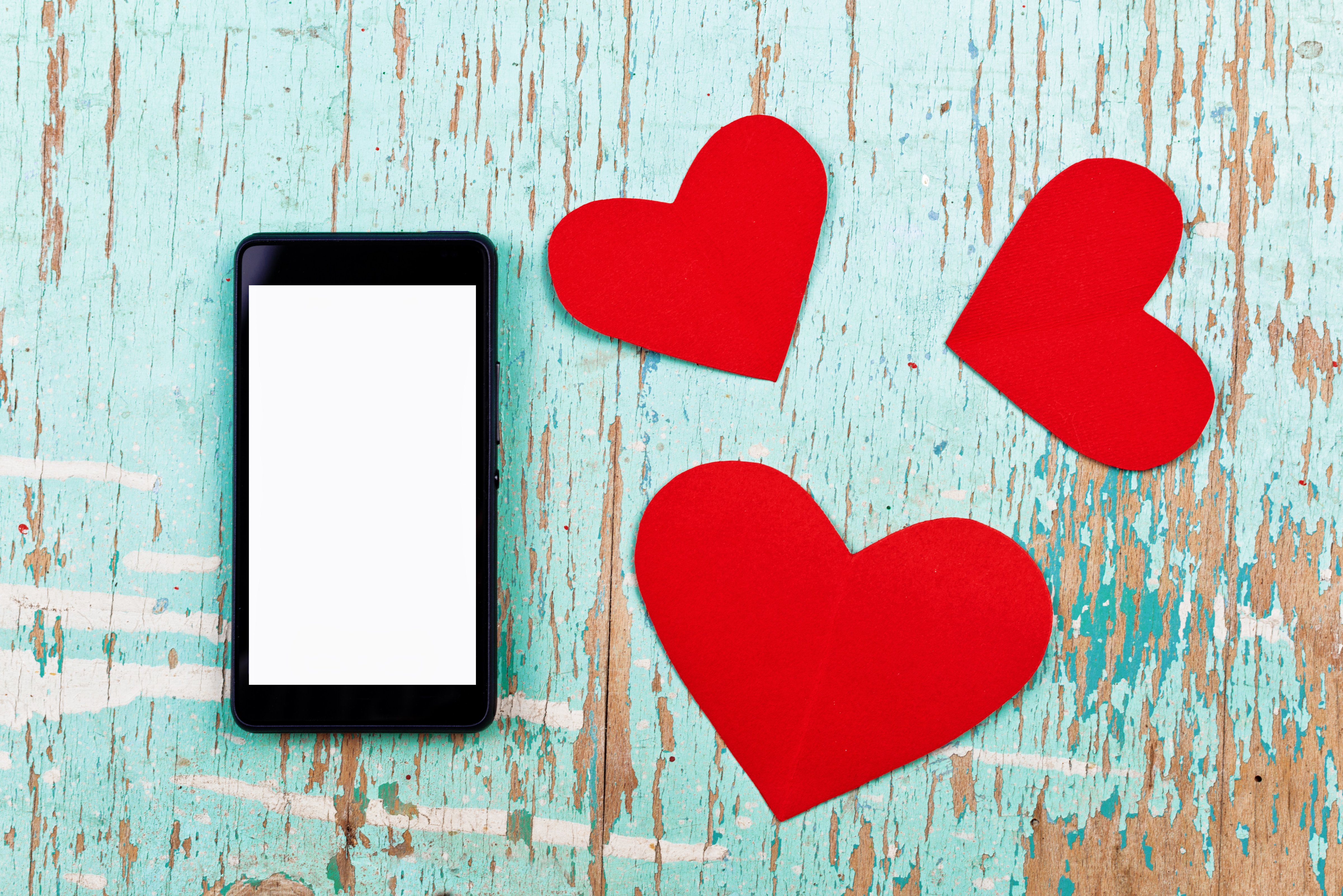 Valentine's Day copy space on smart phone with blank screen and red paper hearts on old grunge wood texture. (stevanovicigor—Getty Images/iStockphoto)