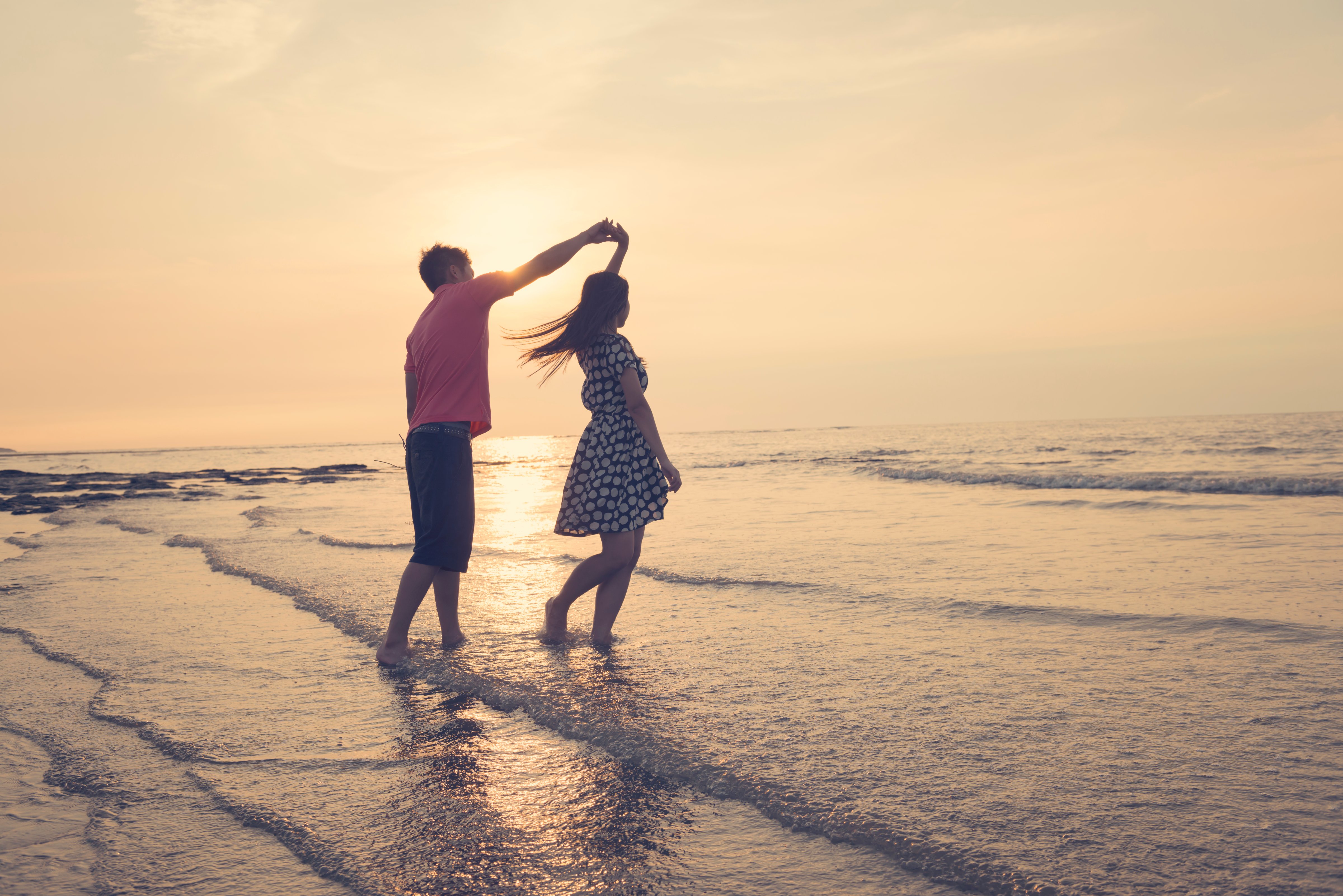 Young couple dancing on beach under sunset.
