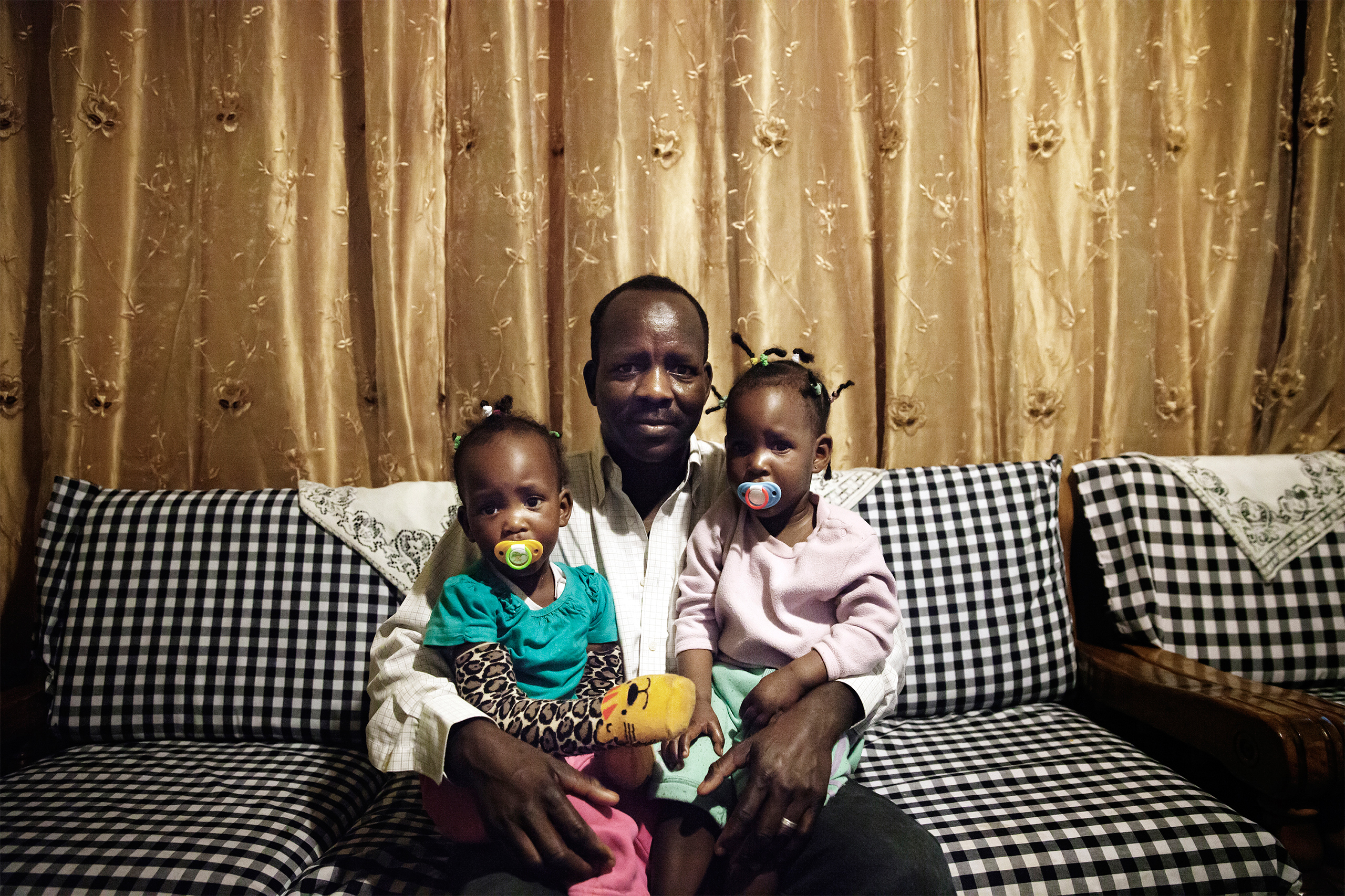 Boshora Adam, an African refugee, appears with his twin daughters in their home in Tel Aviv, Israel.  “The hardest part about raising my children in Israel is that it’s becoming more segregated," he says. "On the playground you notice that parents keep their children away from African children, and this worries me for my children’s future.” (Malin Fezehai)