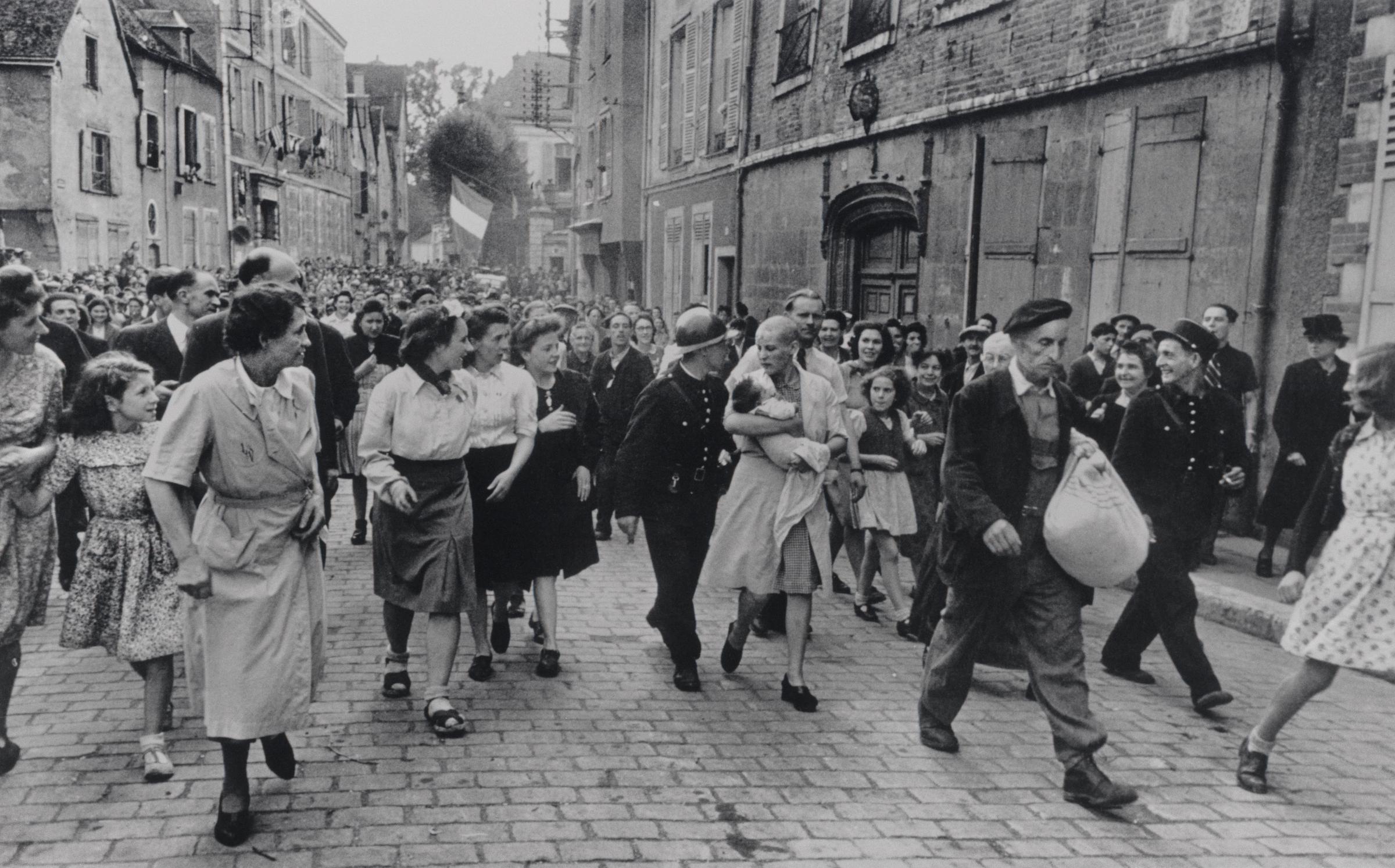 FRANCE. Chartres. August 18th, 1944. French woman, who had had a baby by a Germany soldier, being marched home after being punished by having her head shaved.