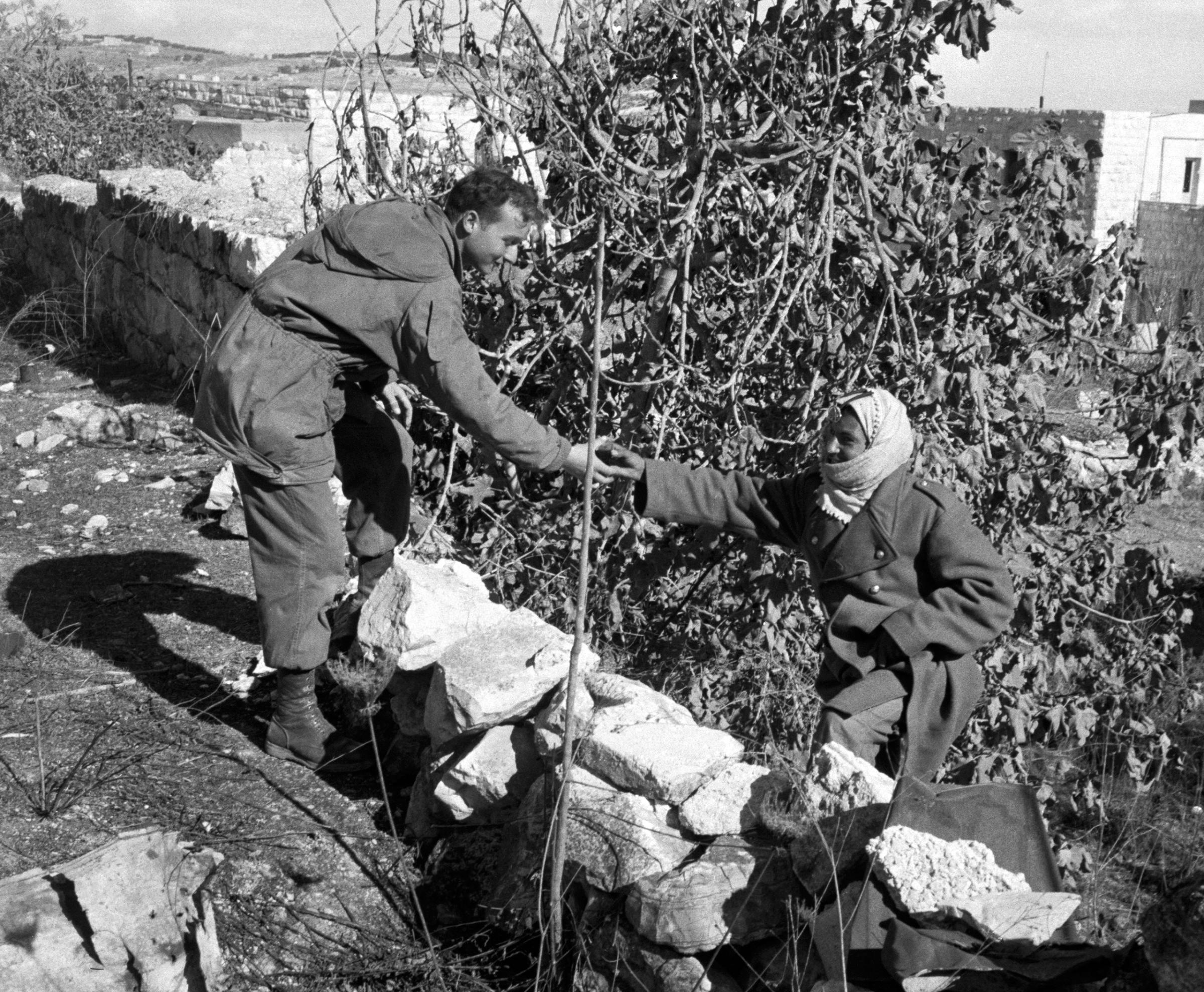 A Jordanian soldier hands a cup of tea to an Israeli paratrooper, at the dividing "Green Line" in Jerusalem, 1956.