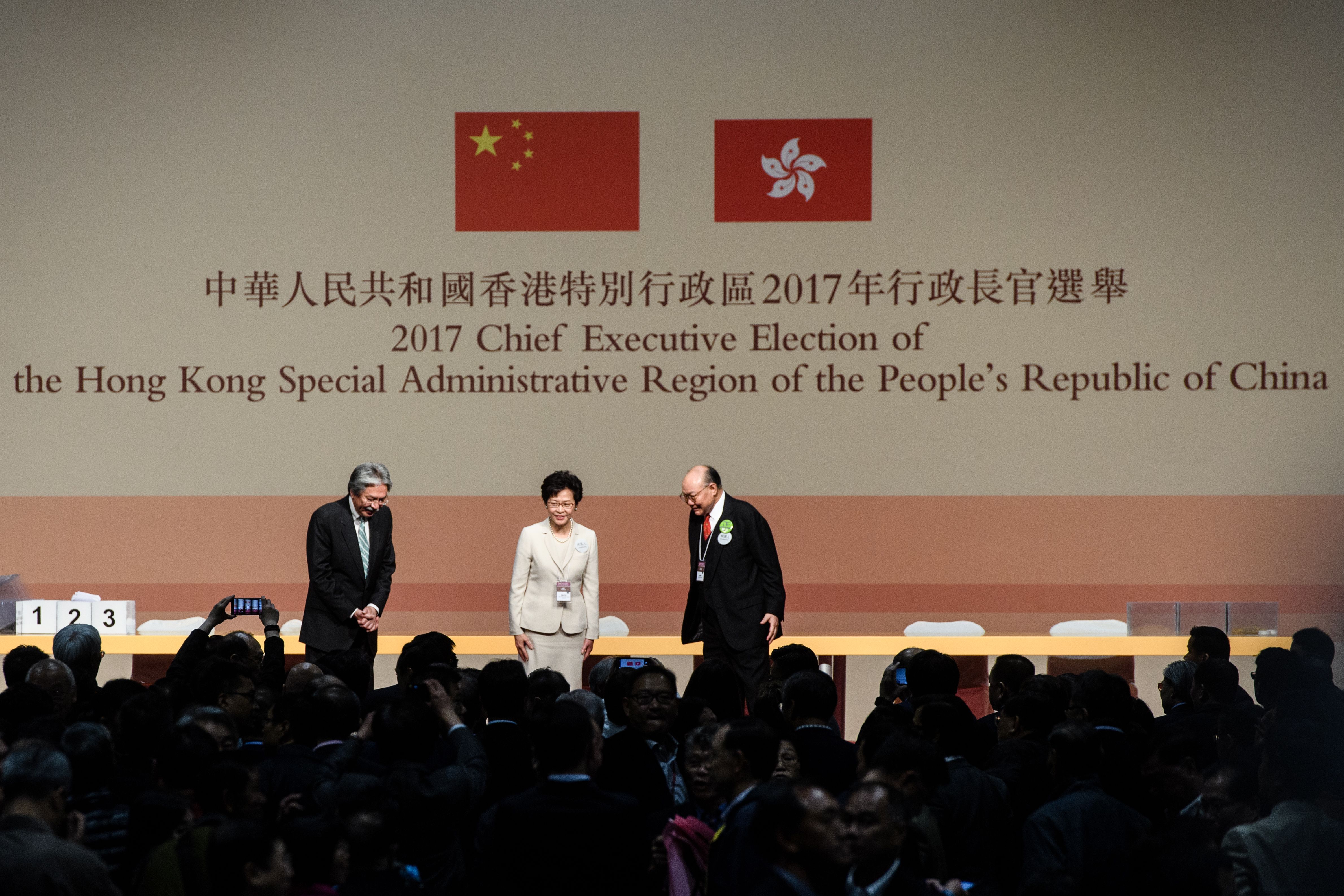 Hong Kong's new Chief Executive Carrie Lam, center, stands on stage with her defeated opponents John Tsang, left, and Woo Kwok-hing, right, in Hong Kong on March 26, 2017 (Anthony Wallace—AFP/Getty Images)