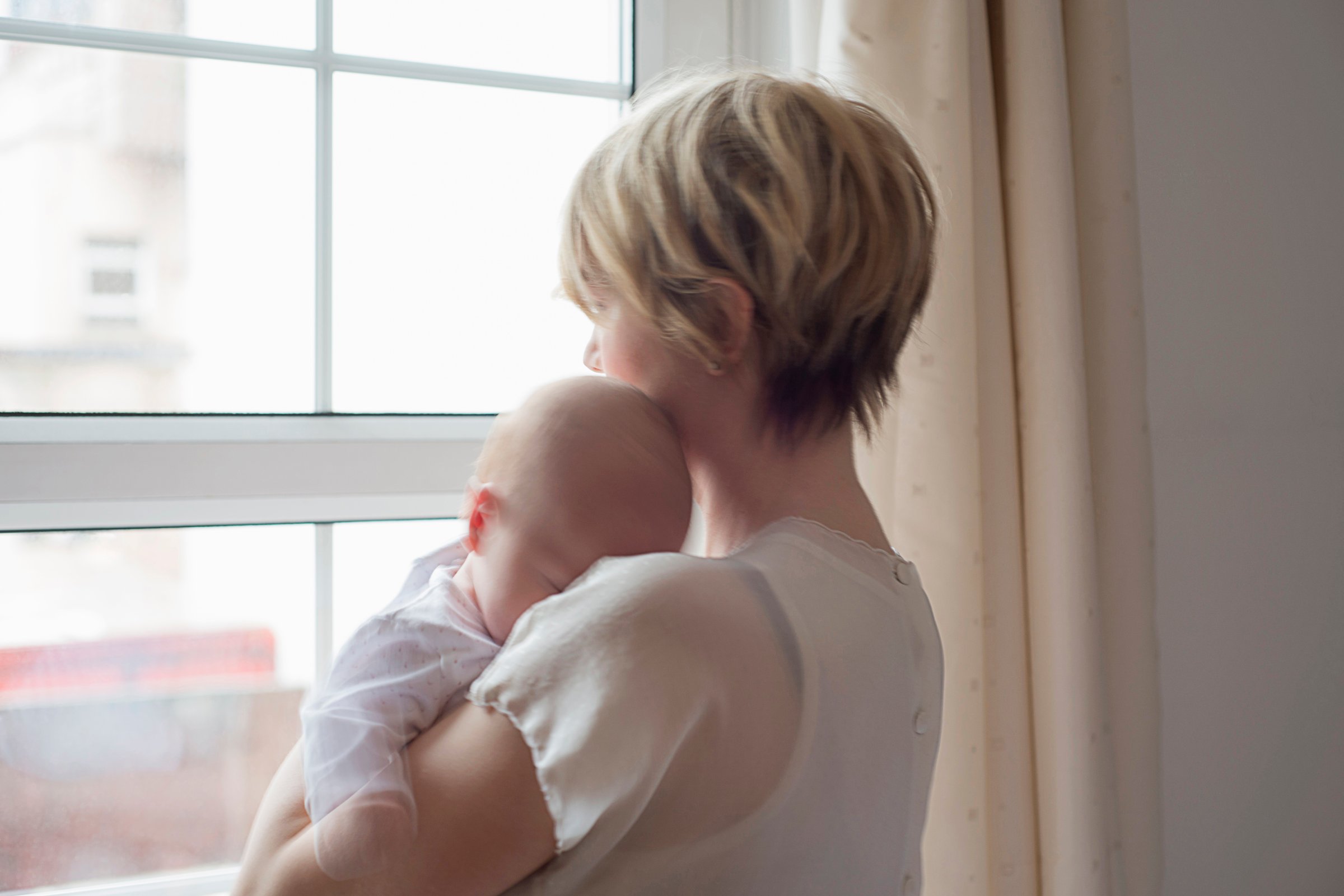 Mother carrying sleeping baby girl, looking out window