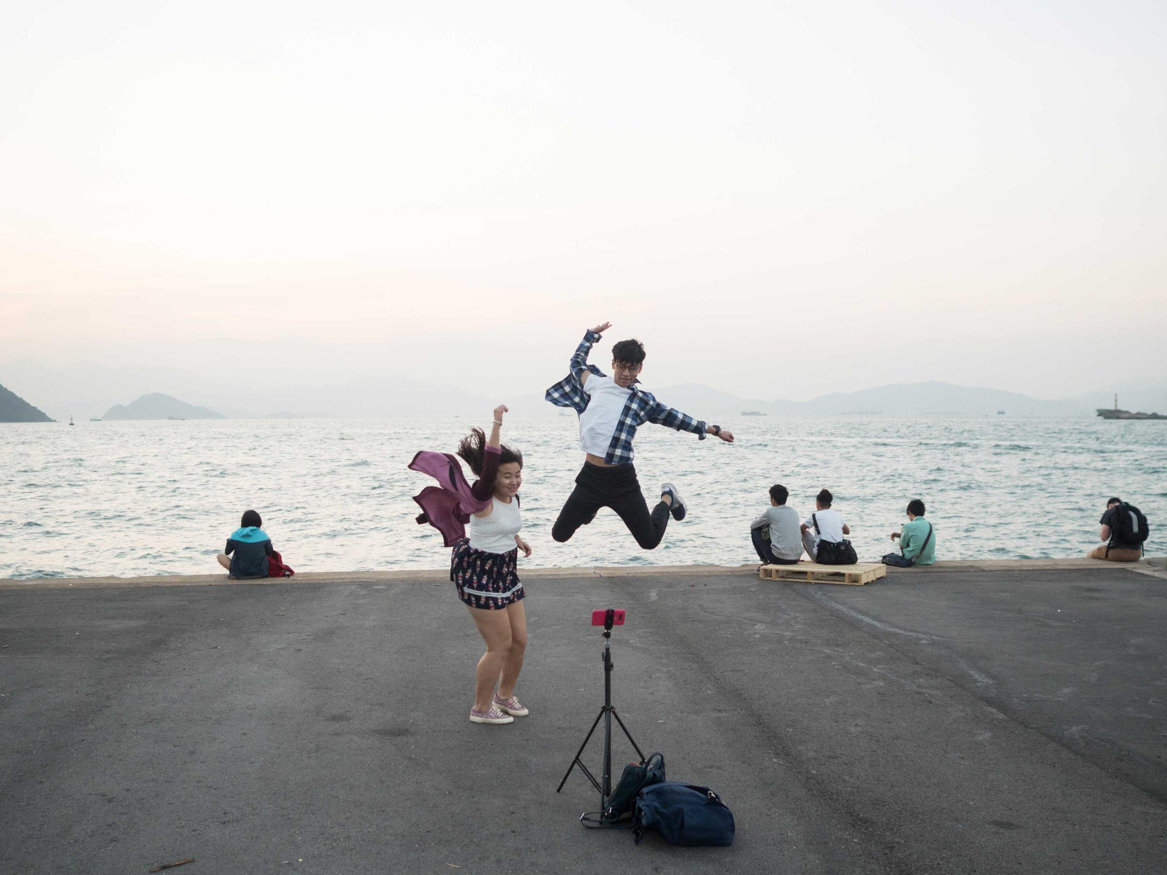 Hong Kong (Hong Kong SAR, China); Date (11, 03, 2016); A young couple practicing jumping in front of the camera; "Instagram pier" is a public cargo pier located on the west side of Hong Kong island; here locals gather for fishing, excercising or walking their pets. More recently the Pier has raised to fame as the “instagram Pier”, where young Hong Kongers and instagrammers come for selfies and scenic photos. I have recently begun curating its "instagram"  dedicated account (@insta_pier).