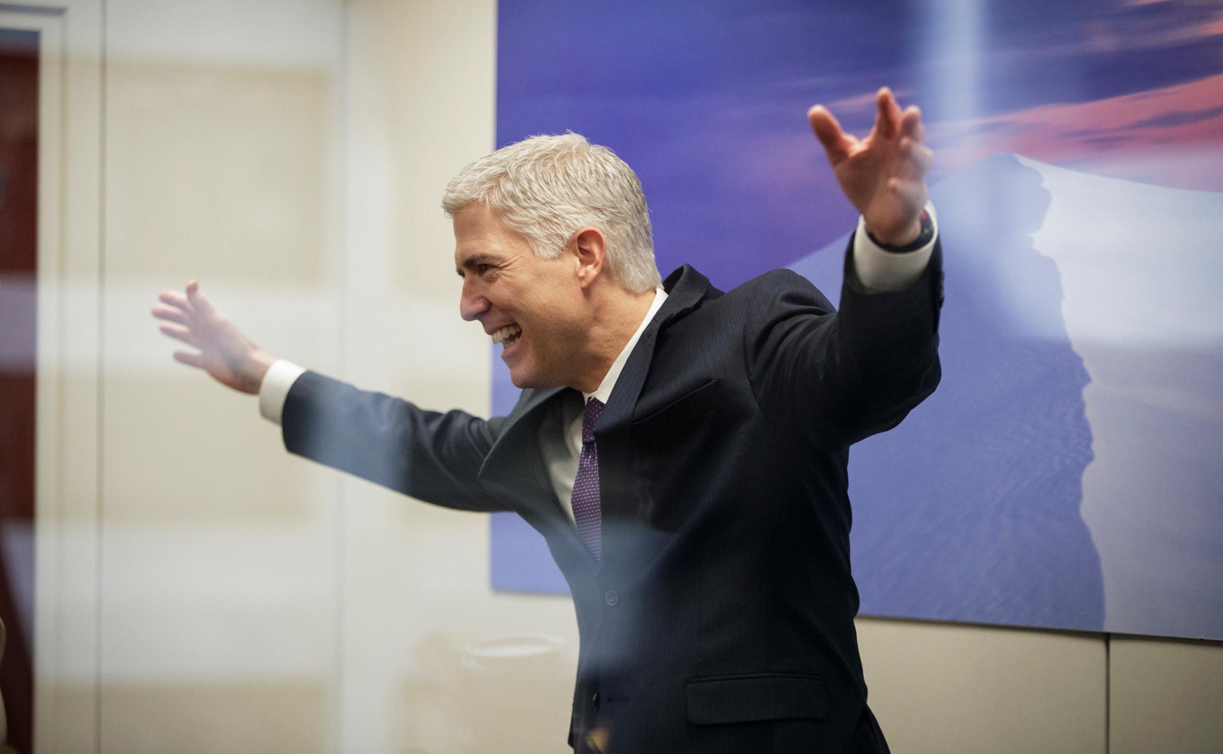 Supreme Court Justice nominee Neil Gorsuch, seen through glass, makes an animated gesture while speaking with staff members before his meeting with Sen. Tom Udall, D-N.M., Feb. 27, 2017, on Capitol Hill in Washington. D.C.