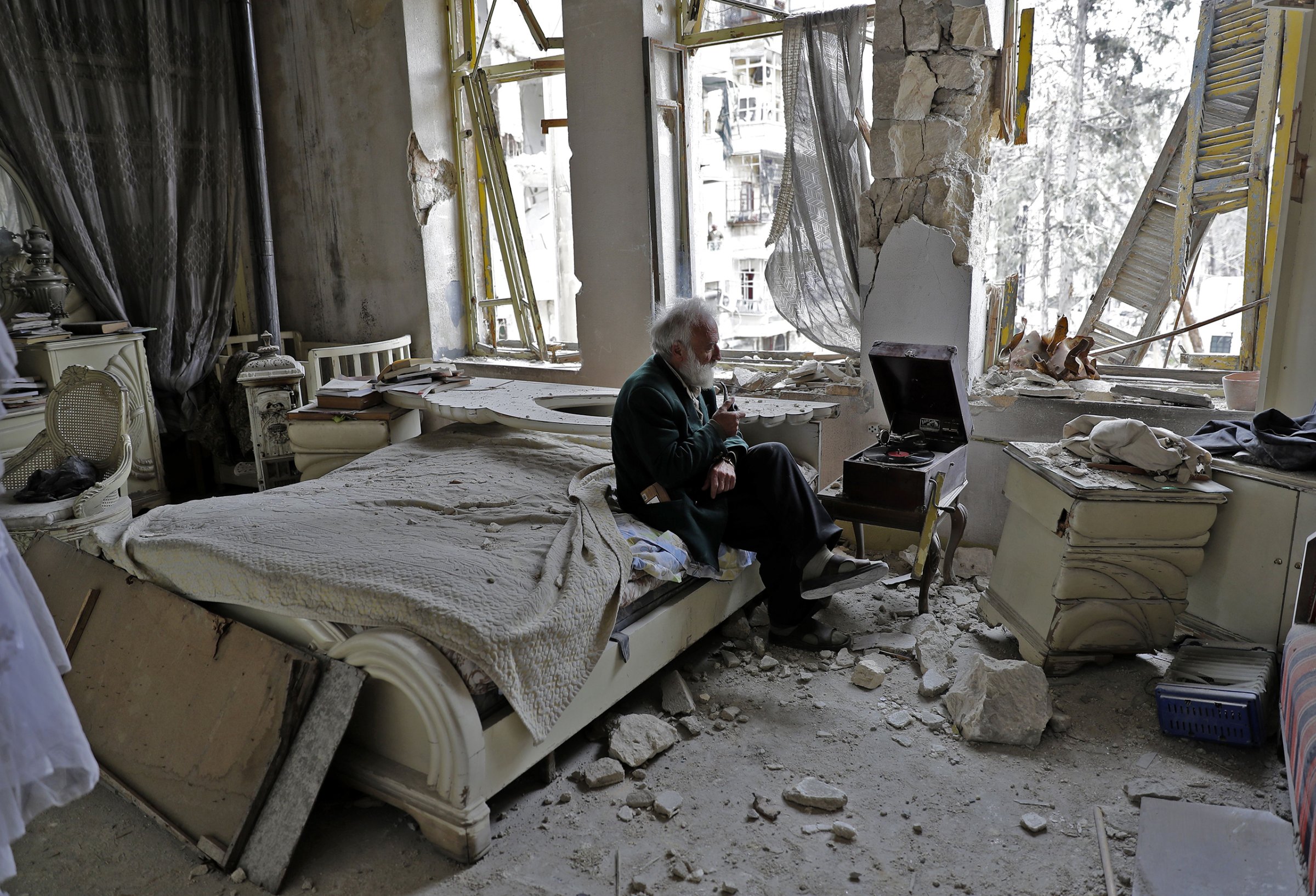 A man smokes his pipe as he sits in his destroyed bedroom, listening to music, in Aleppo's formerly rebel-held neighborhood of al-Shaar on March 9, 2017.