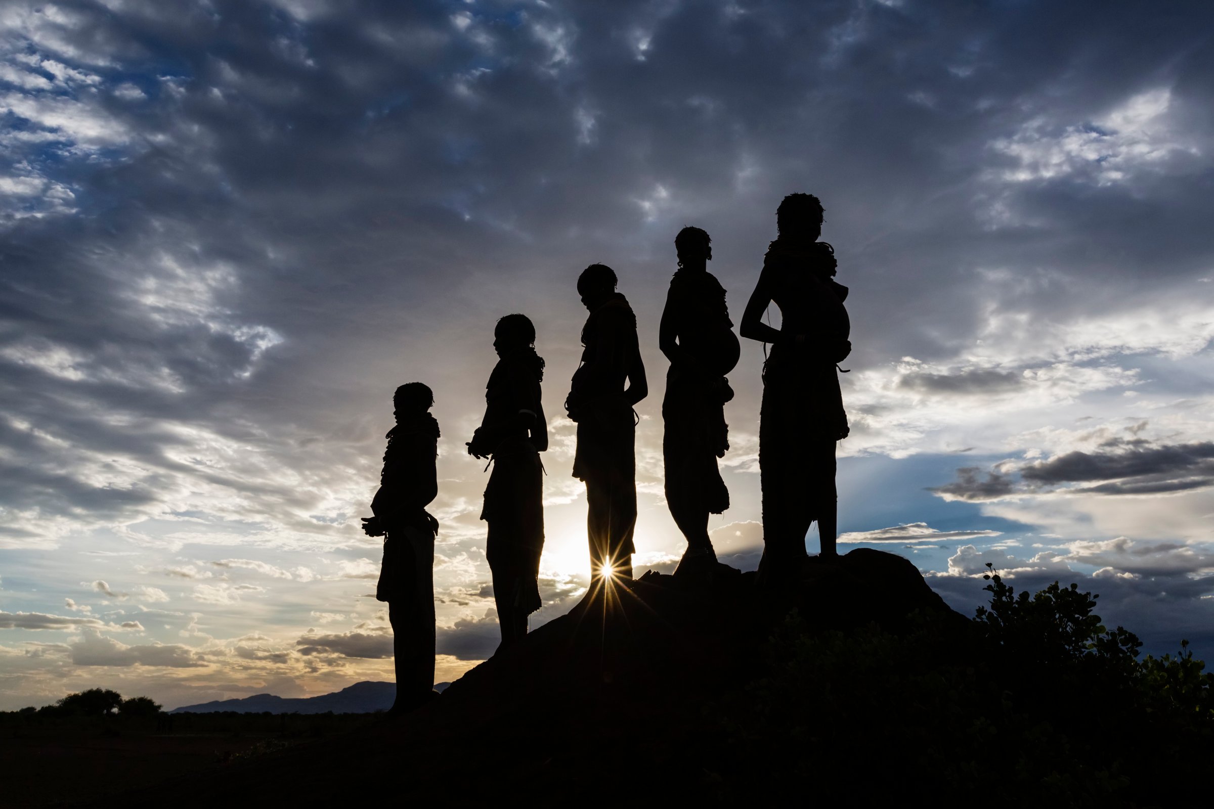 Silhouettes of pregnant woman under cloudy sky at sunset, Nyangaton, Ethiopia