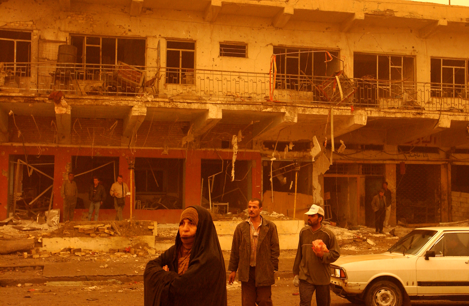 During a sandstorm, Iraqis stand in front of wreckage of a building in the days following the U.S. bombing campaign, Baghdad, Iraq, March 26, 2003.