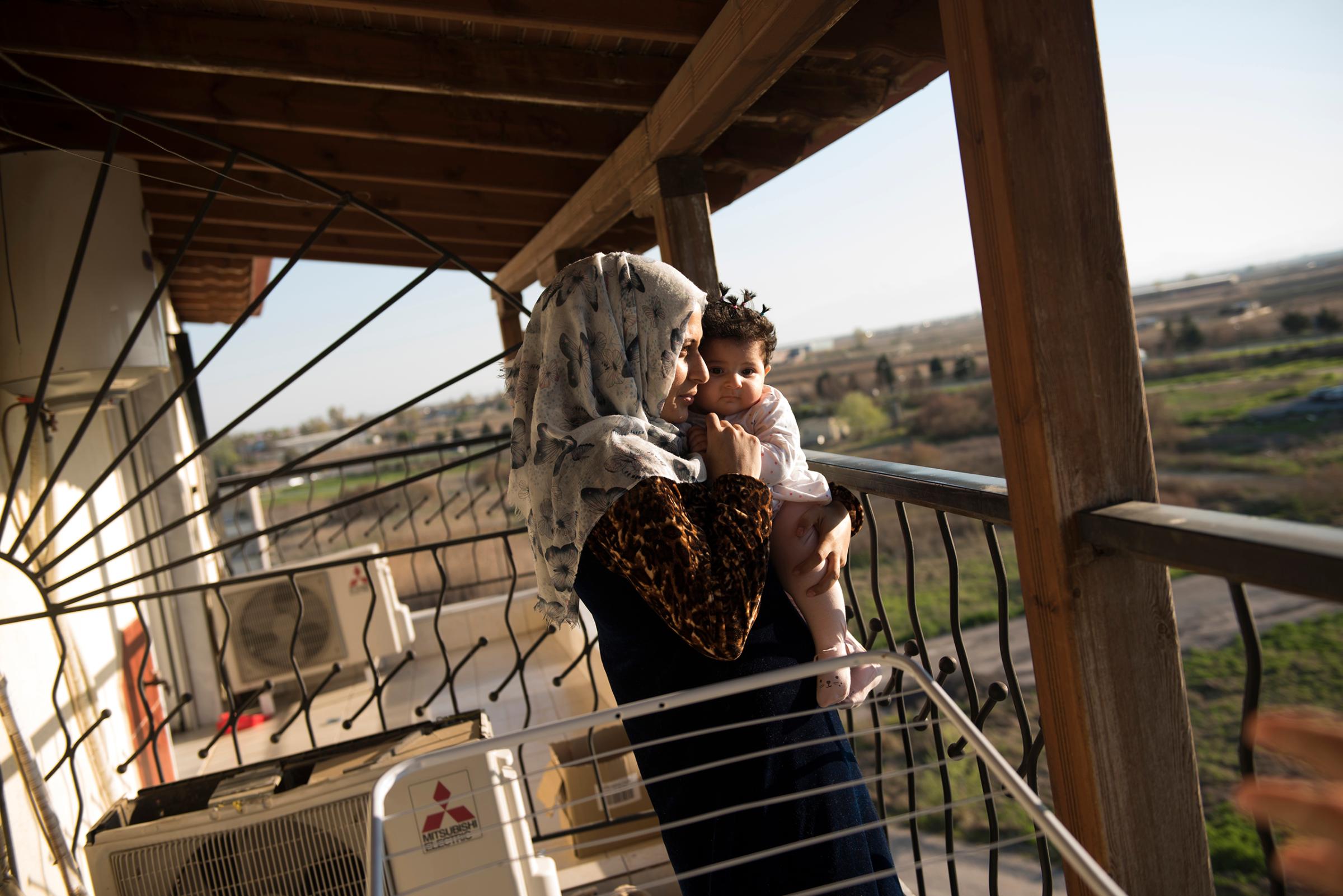 Noor Al Talaa, 22, stands on the balcony at dusk with baby Rahaf, almost 6 months, at an apartment in Sidros, outside of Thessaloniki, Greece, March 28, 2017.