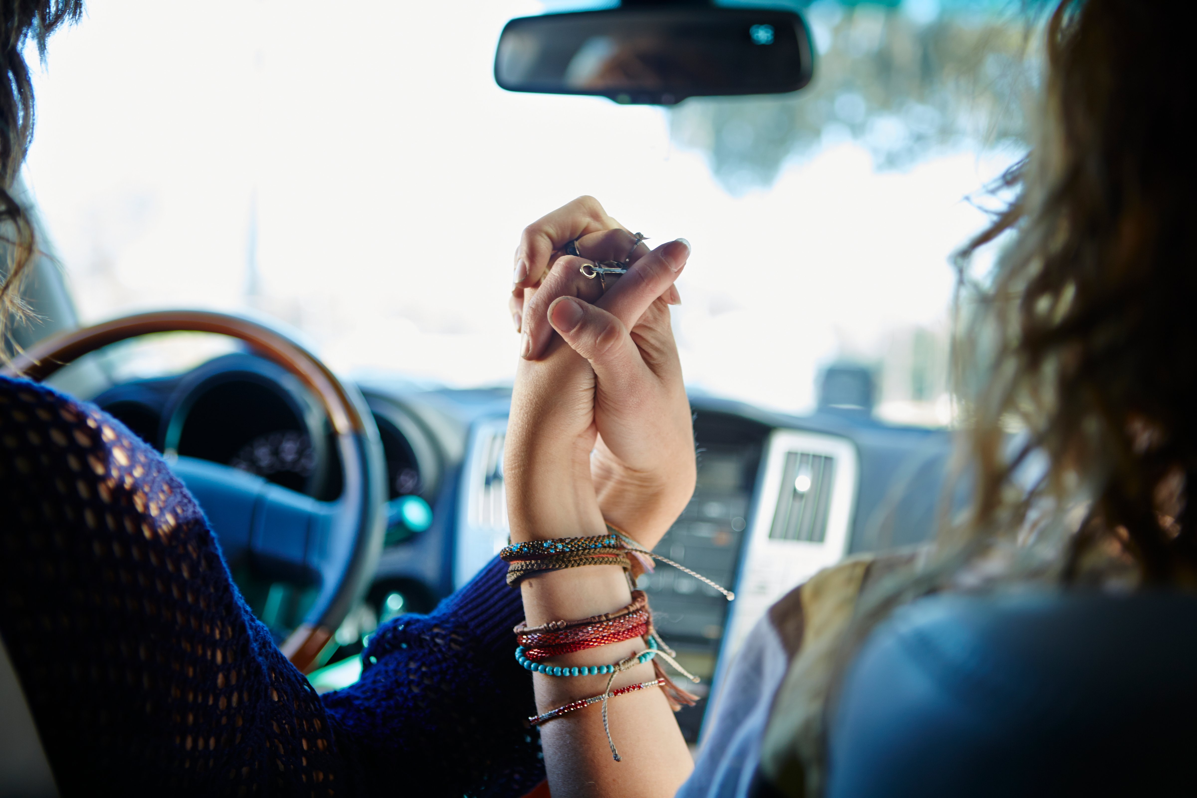 Two young women holding hands in car