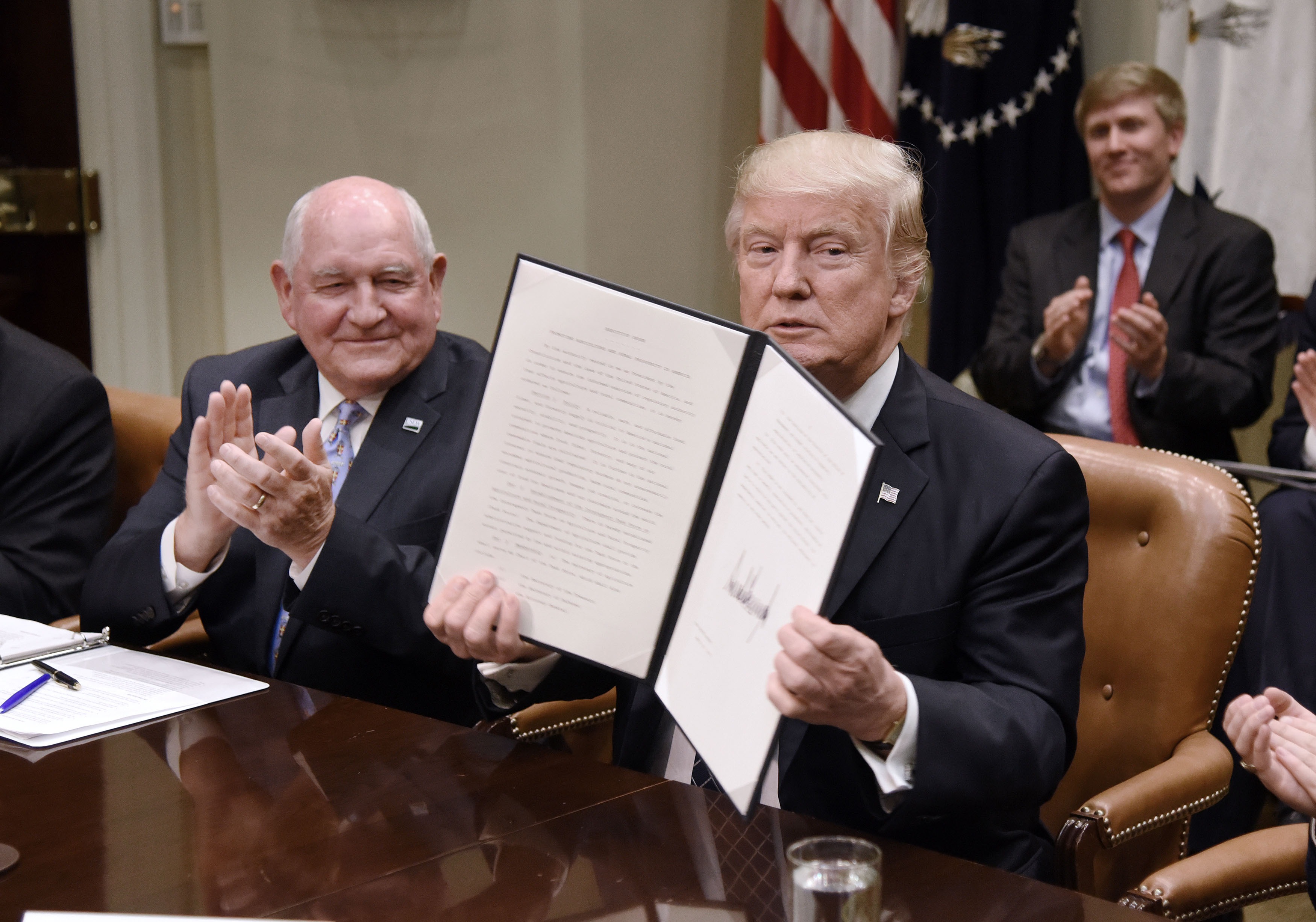 President Donald Trump signs the Executive Order Promoting Agriculture and Rural Prosperity in America as Agriculture Secretary Sonny Perdue looks on during a roundtable with farmers in the Roosevelt Room of the White House on April 25, 2017 in Washington, DC. (Photograph by Olivier Douliery—Getty/Pool)