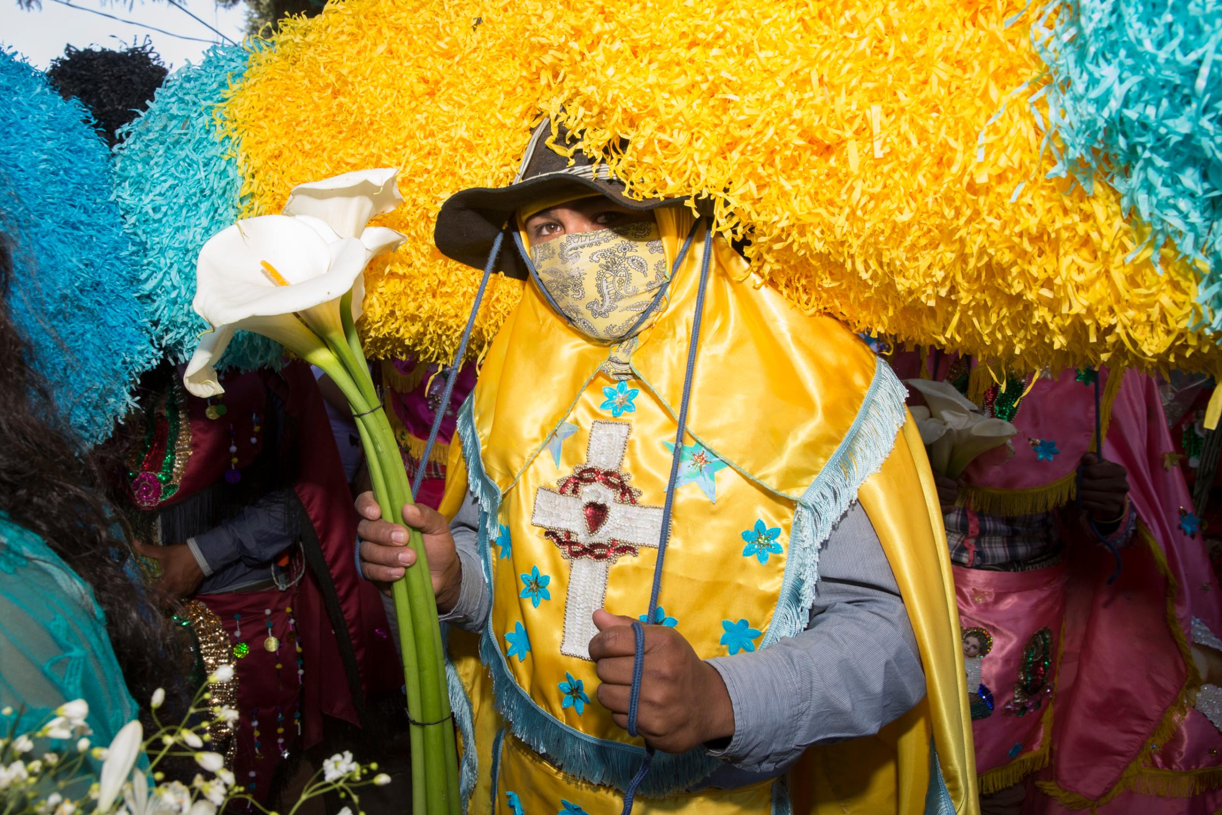 A young man dressed as a Sayone holds a flower during the Sunday procession of Holy Week in Tetela del Volcan, Morelos, Mexico. The Sayones, impersonate the Roman soldiers who killed Jesus. They wear brightly colored costumes with figures of saints, hold machetes, wear goat skin leather mask and paper hats. After the mass that ends Holy Week on Sunday people throw lit matches at them to set their hats on fire, in sign of vengeance for their murderous act.