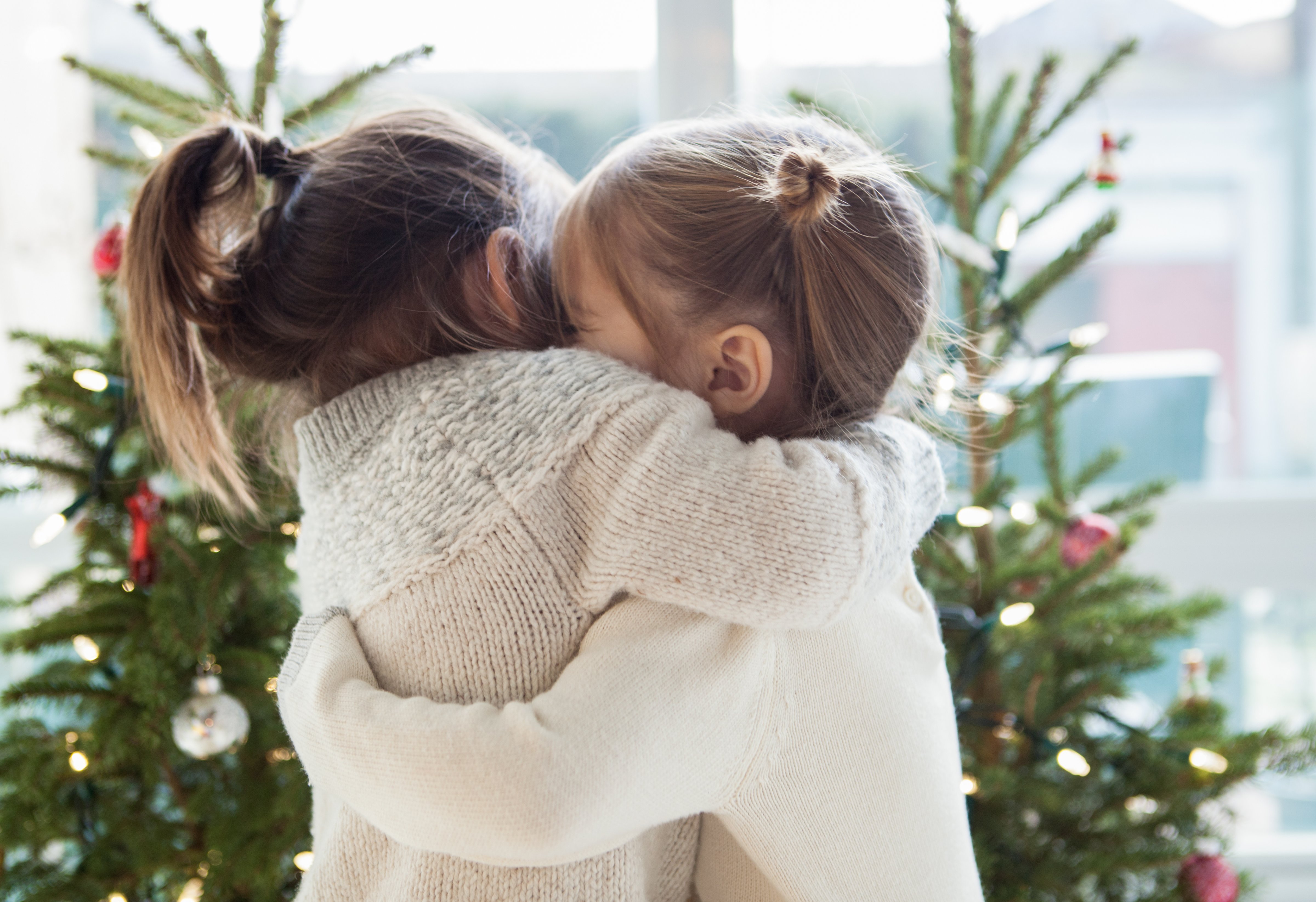 Girls hugging in front of Christmas trees