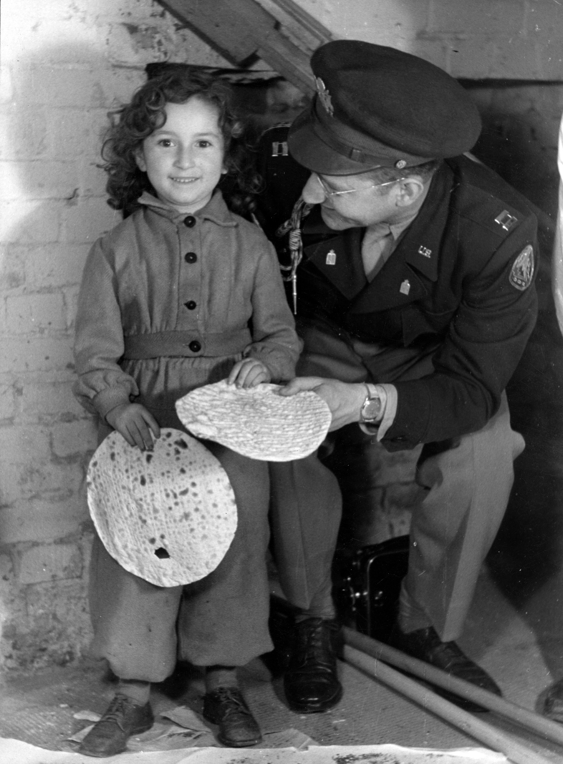 A young girl from the Berlin-Mariendorf DP Camp holding a round shmurah matzah. With her is Captain J. Robbins, Jewish Chaplain for Berlin. Berlin-Mariendorf, Germany, c. 1947