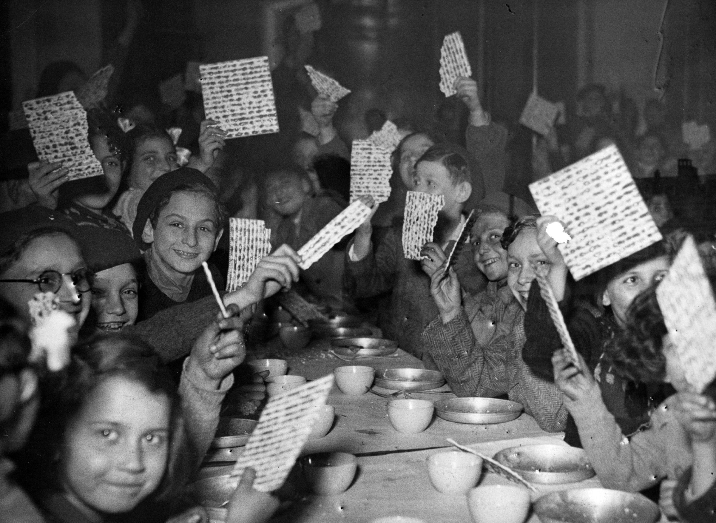 Young refugees at a Passover Seder holding up their matzot with pride at a children's canteen run by the JDC partner Federation des Societes Juives en France. France, c. 1947. Photographer unknown.