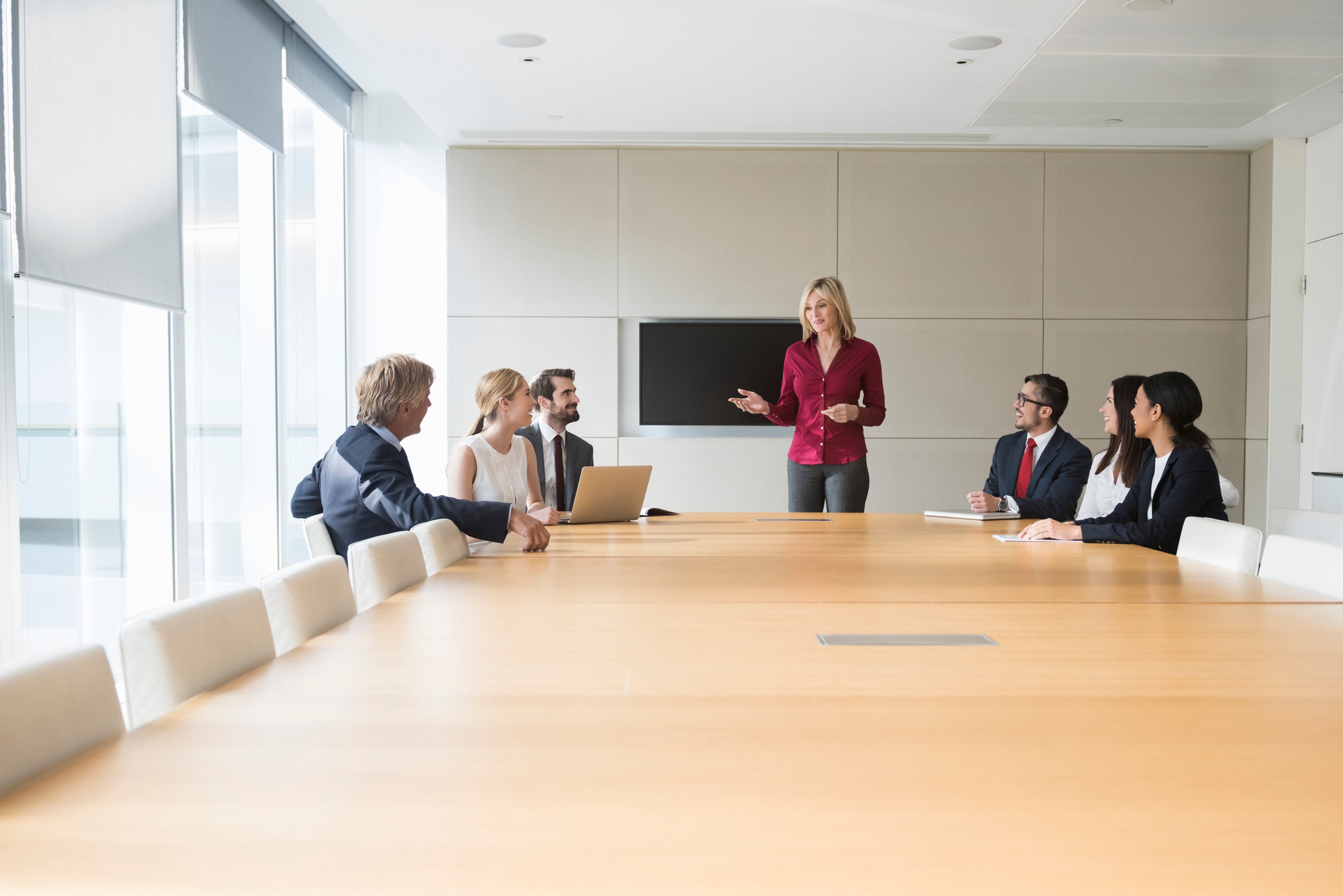 A photo of businesswoman giving presentation to colleagues at conference table. Professionals are in formals. Business people are in board room. Concentrated associates listening to presentation, in a brightly lit modern office. (Getty Images)