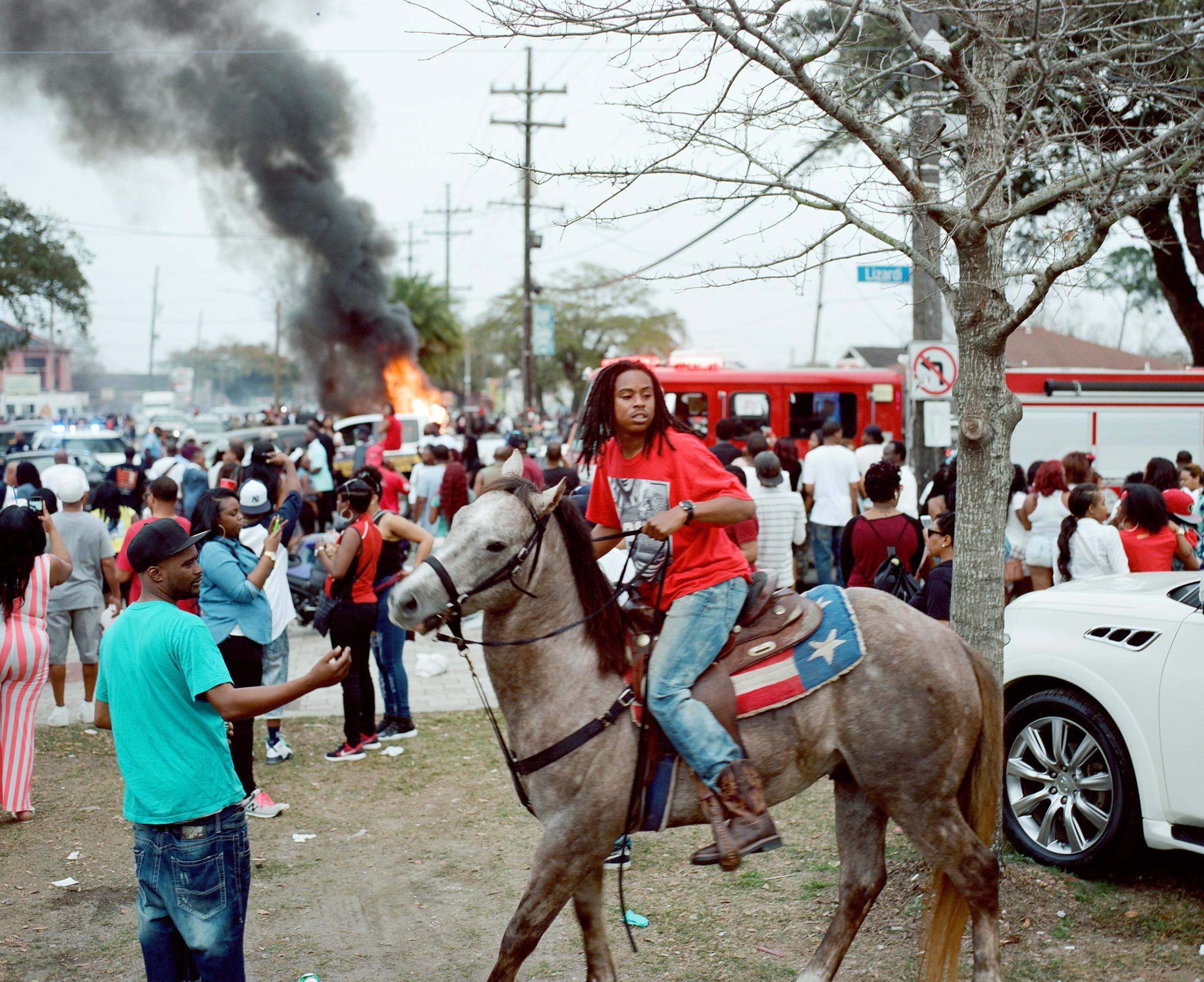 A young man on horseback at a Second Line moves away from a burning car in Holy Cross, Louisiana. 2016