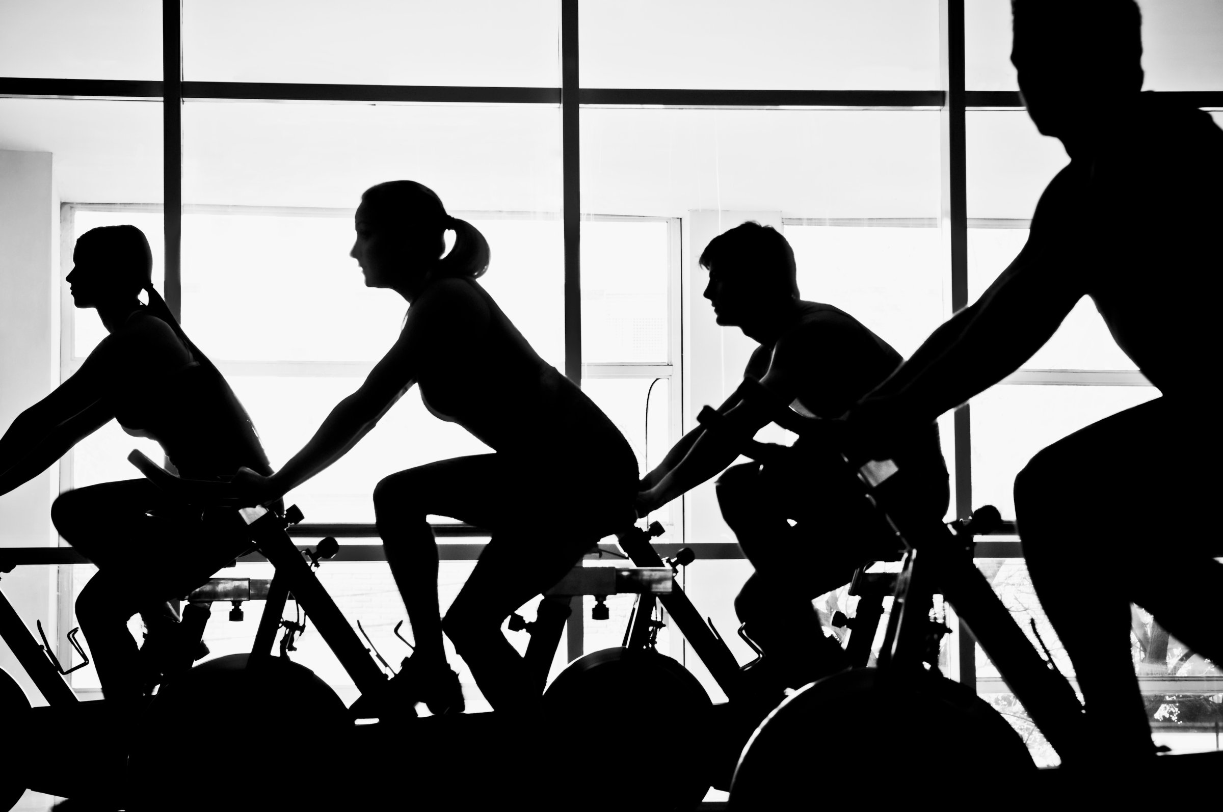 Silhouette of four people working out on exercise bikes in a gym