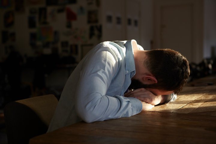 Young man sitting at kitchen table with his head down TIME health stock