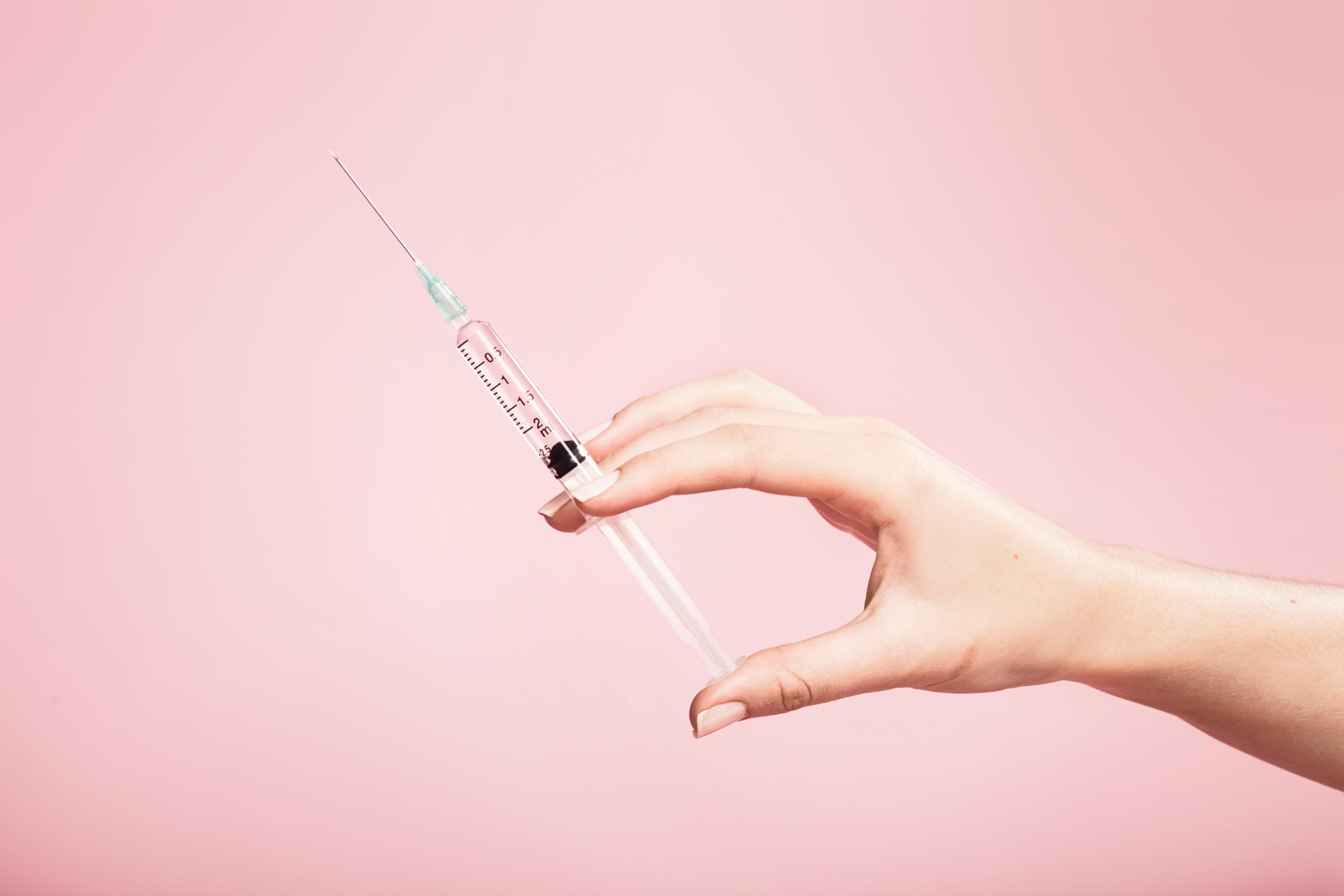 Hand holding syringe in plain pink background TIME health stock