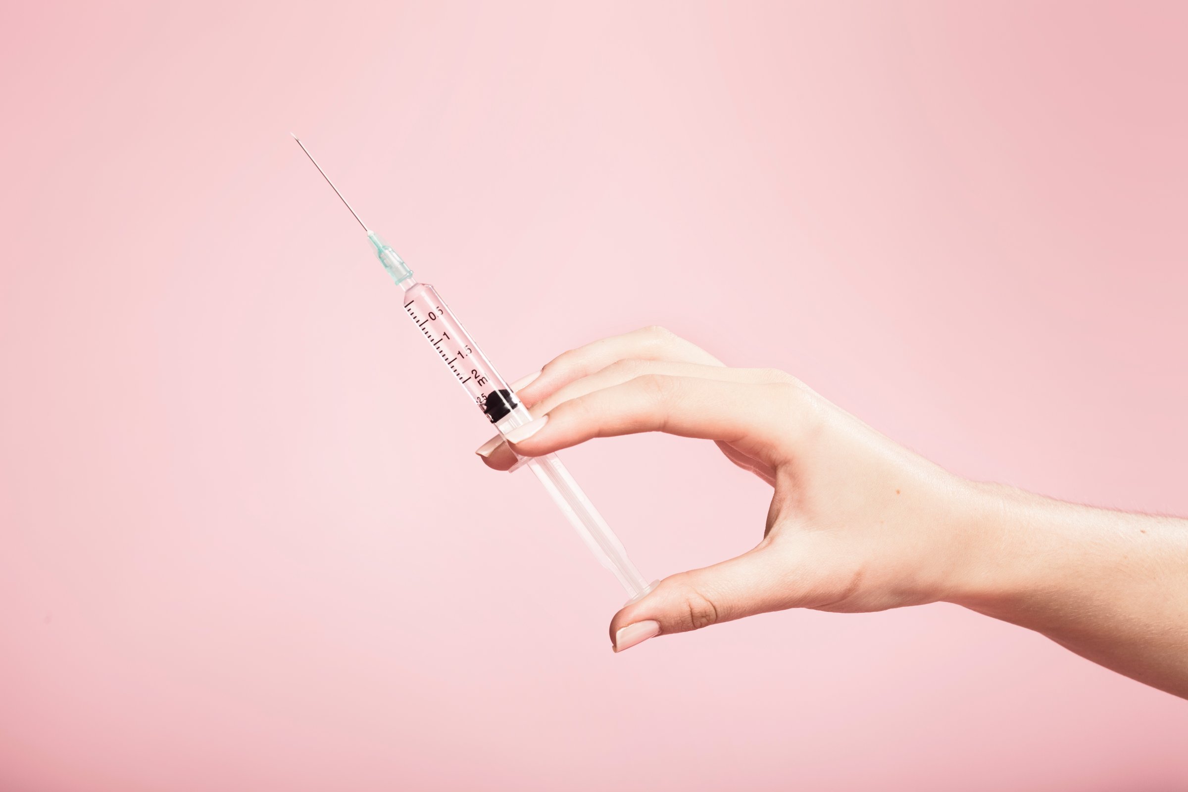 Hand holding syringe in plain pink background