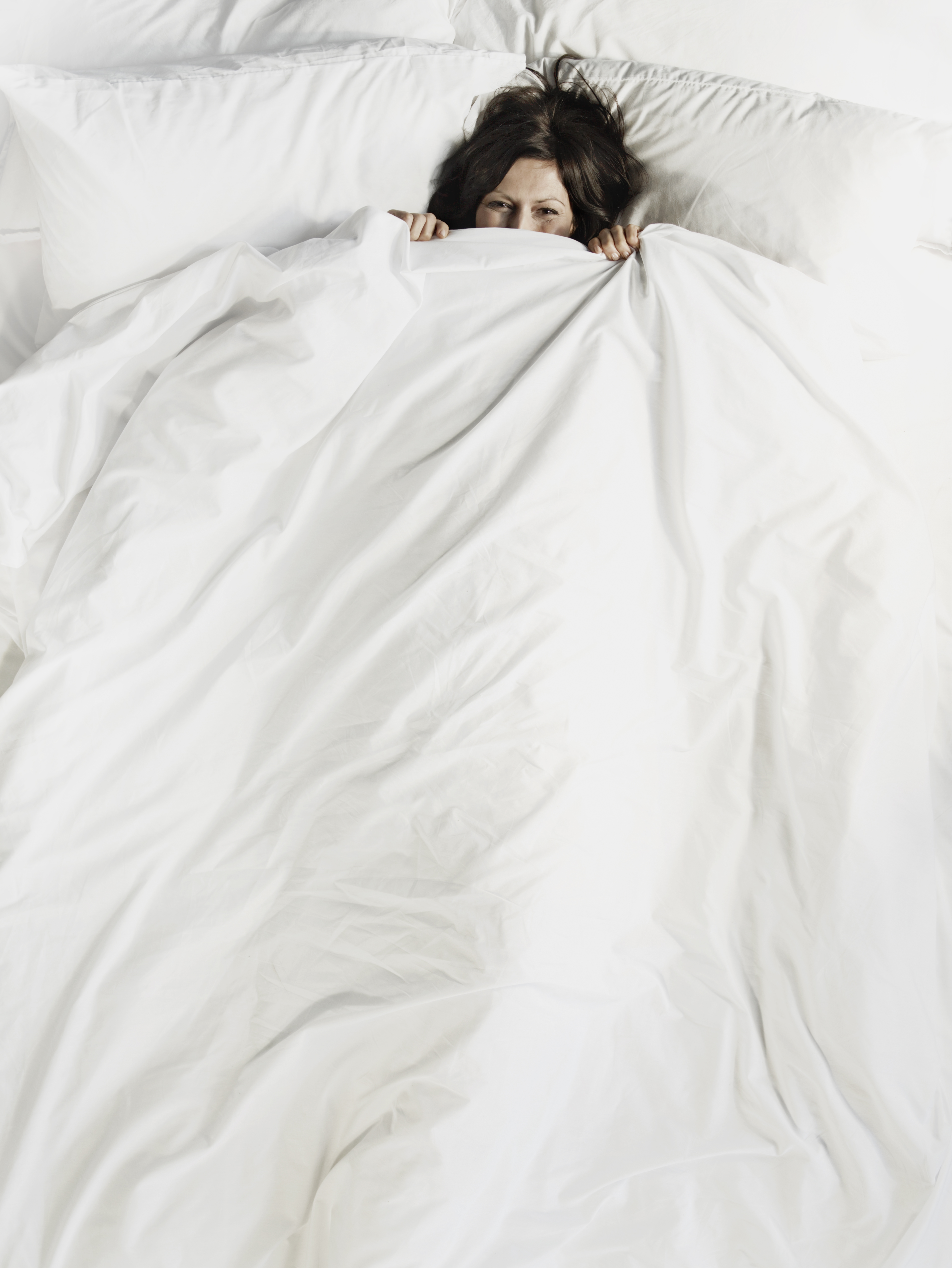 Woman peering over the top of bed sheet