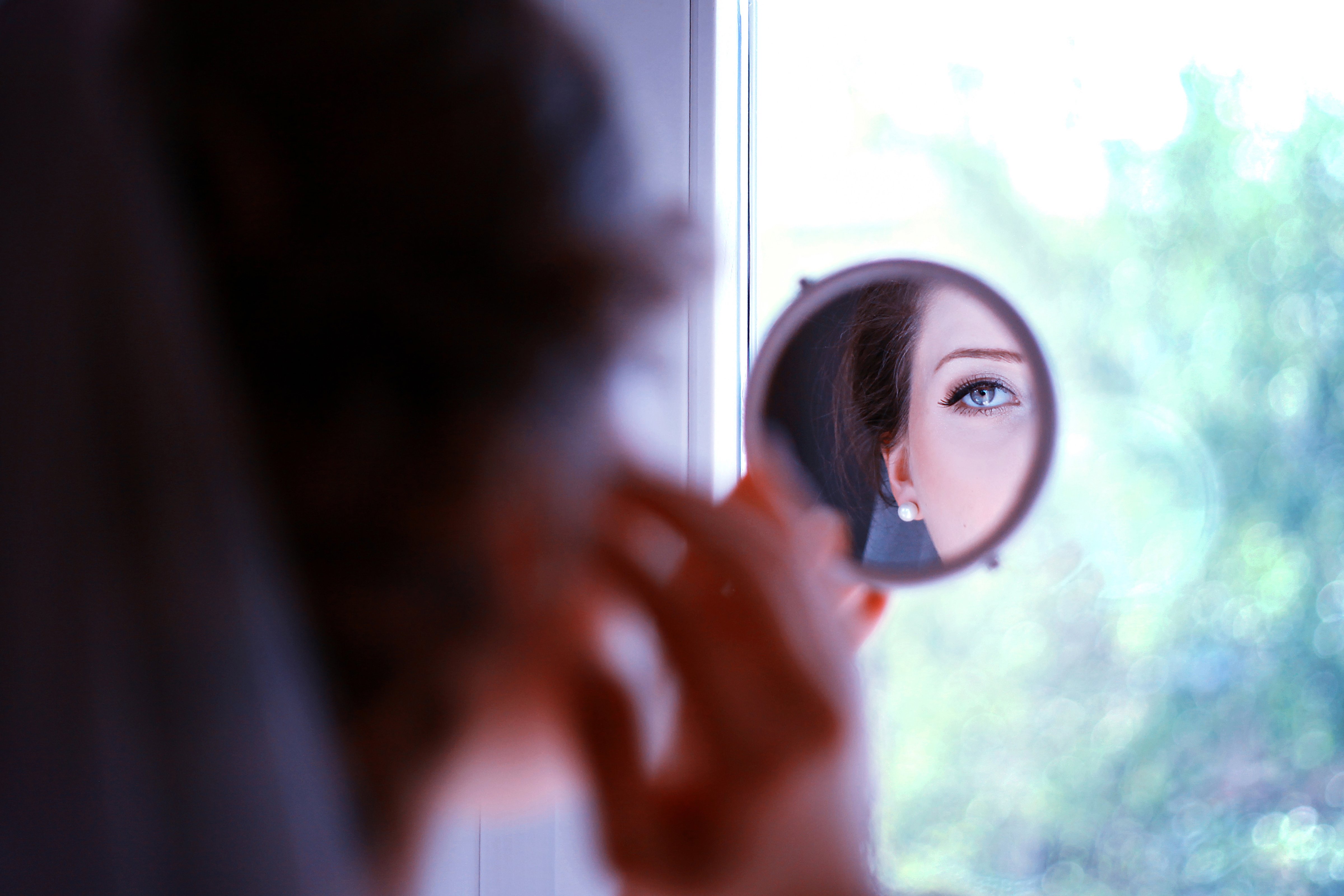 Beautiful young woman looking into a hand mirror