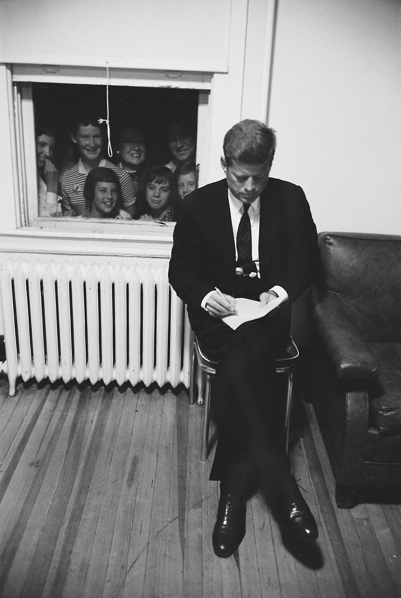 John F. Kennedy prepares a speech as admirers watch from outside a window, Baltimore, September 1960.