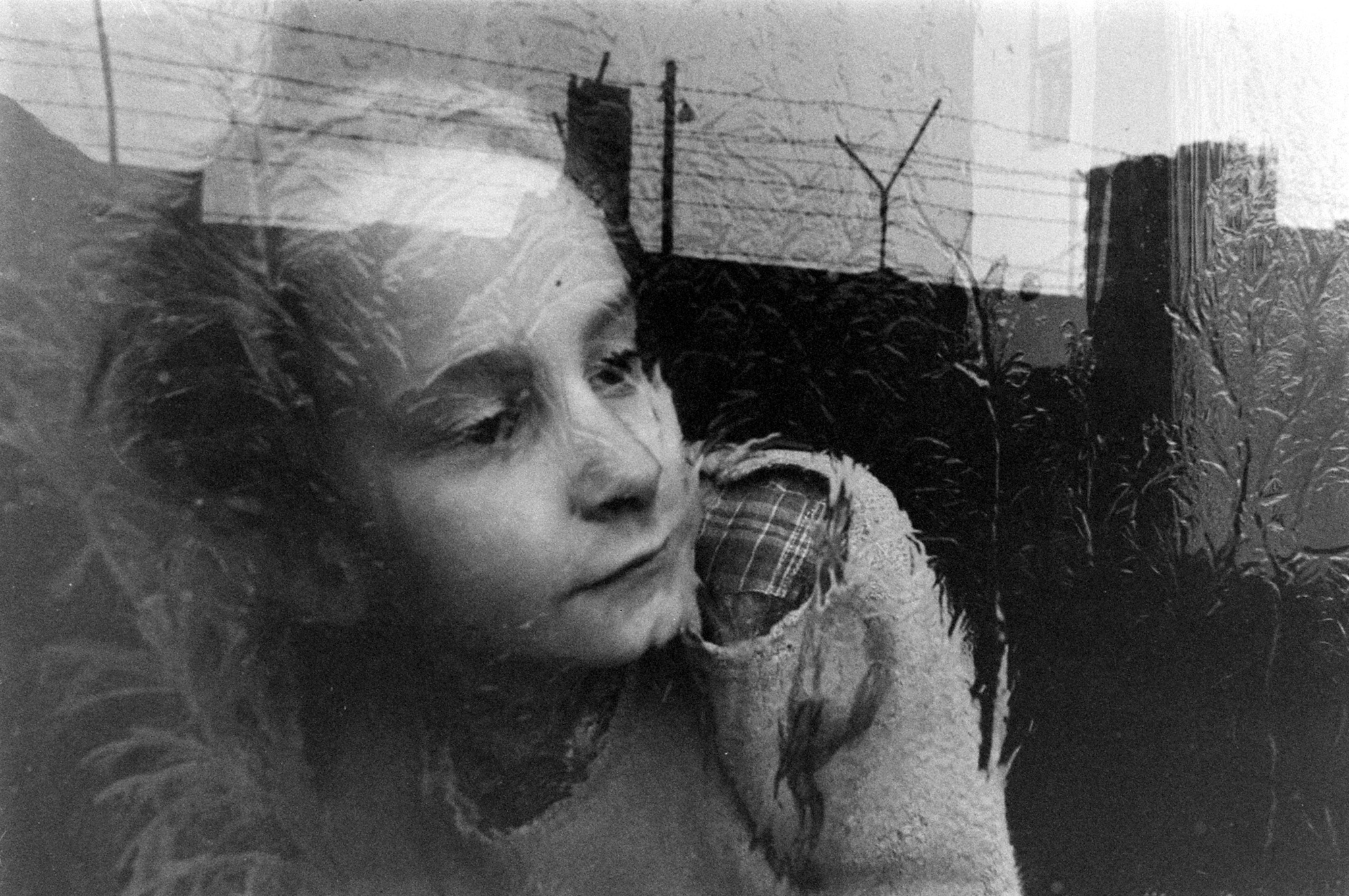 A young girl gazes through her apartment window which looks out on barbed wire fencing that tops the nearby Berlin wall, December 1962.