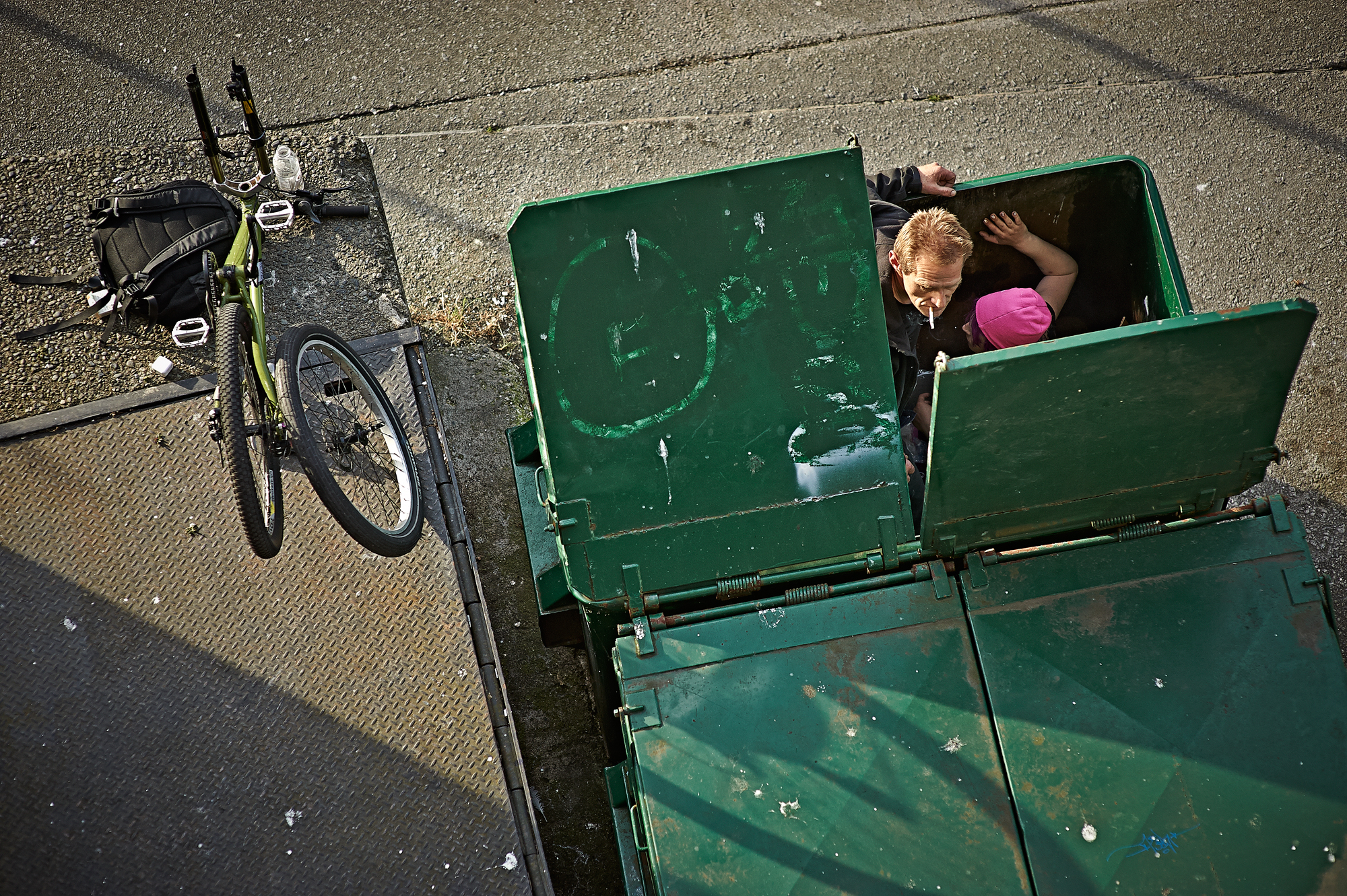 A man looks over his shoulder while being serviced in the dumpster. July, 2014.