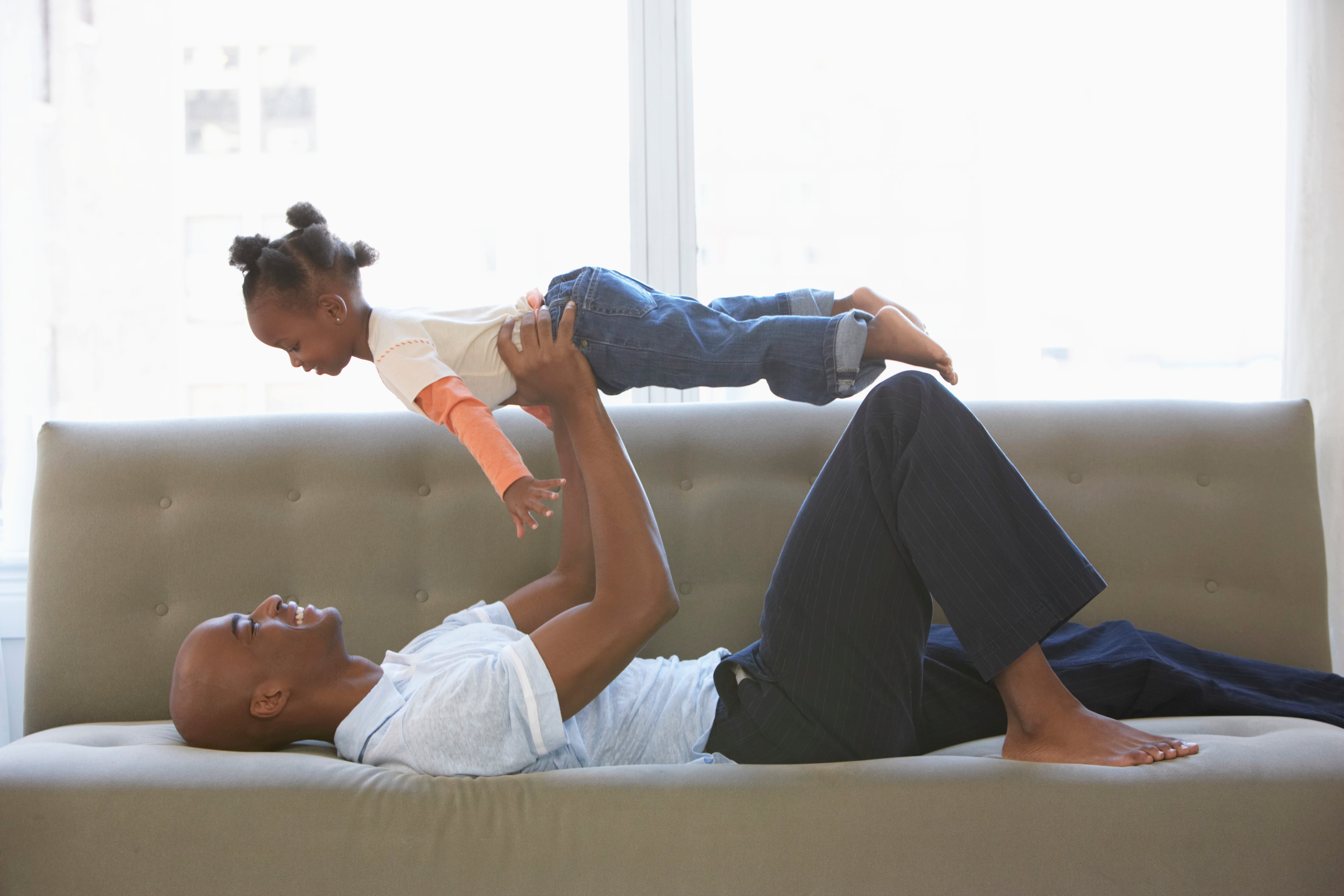 Father lying on sofa, holding daughter (2-4) up (Christopher Robbins&mdash;Getty Images)