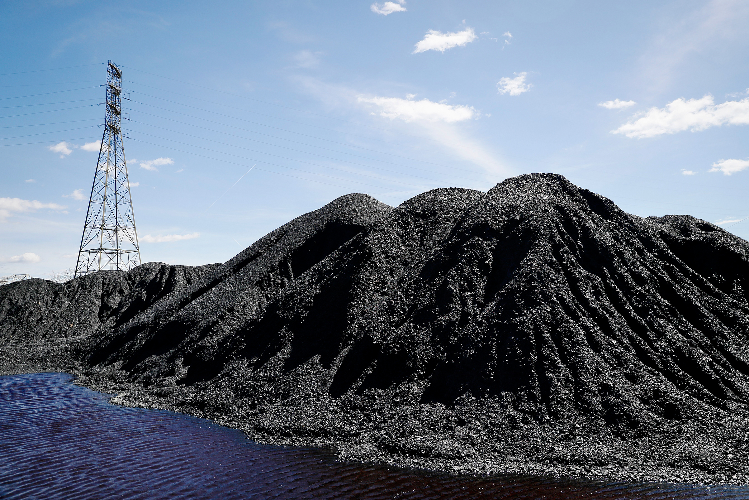 Power lines loom behind piles of coal stored at a facility along the Ohio River in April (John Minchillo—AP)