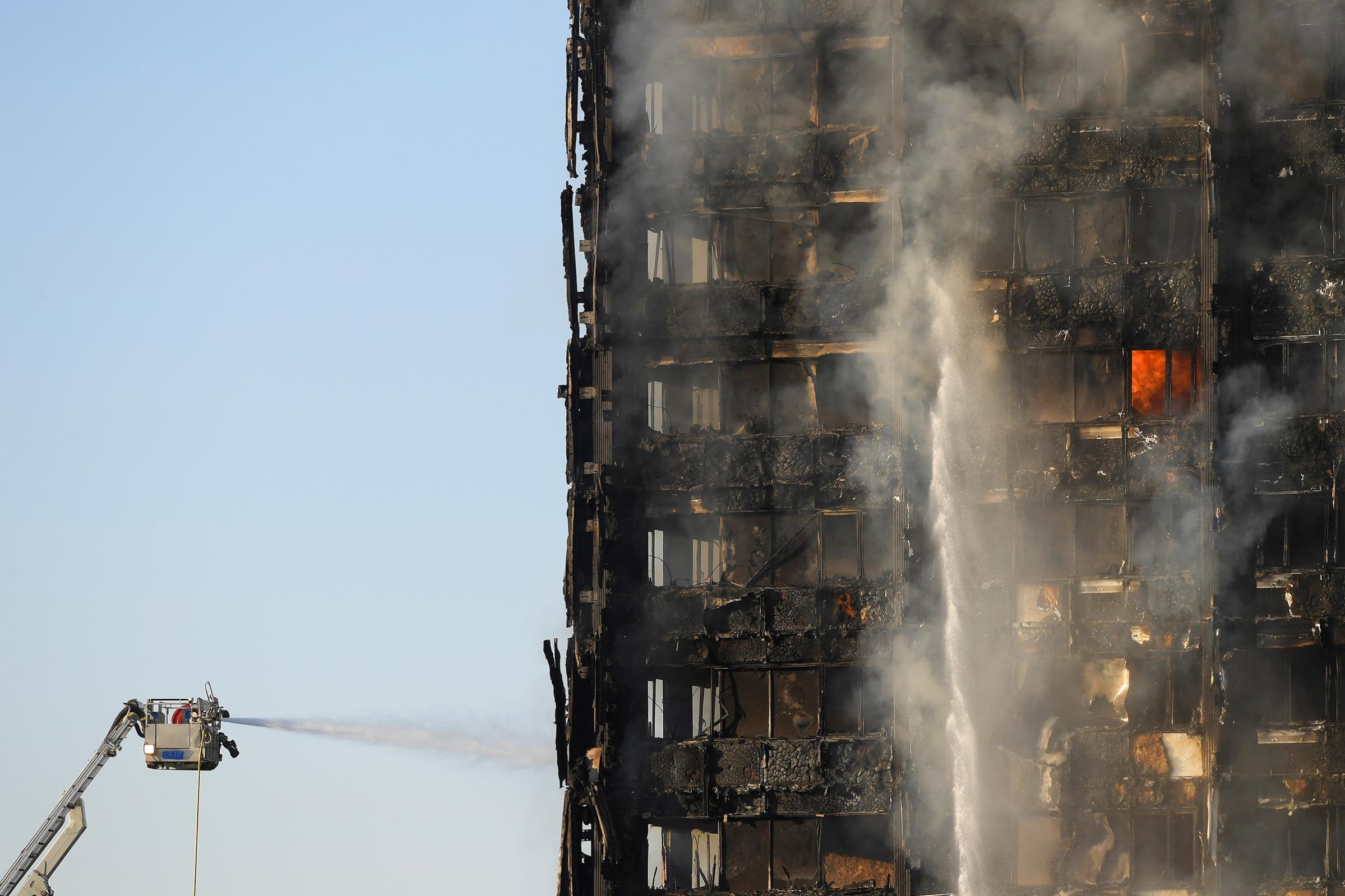 Firefighters spray water into the smoldering frame of a high-rise that caught fire overnight in West London on June 14, 2017.