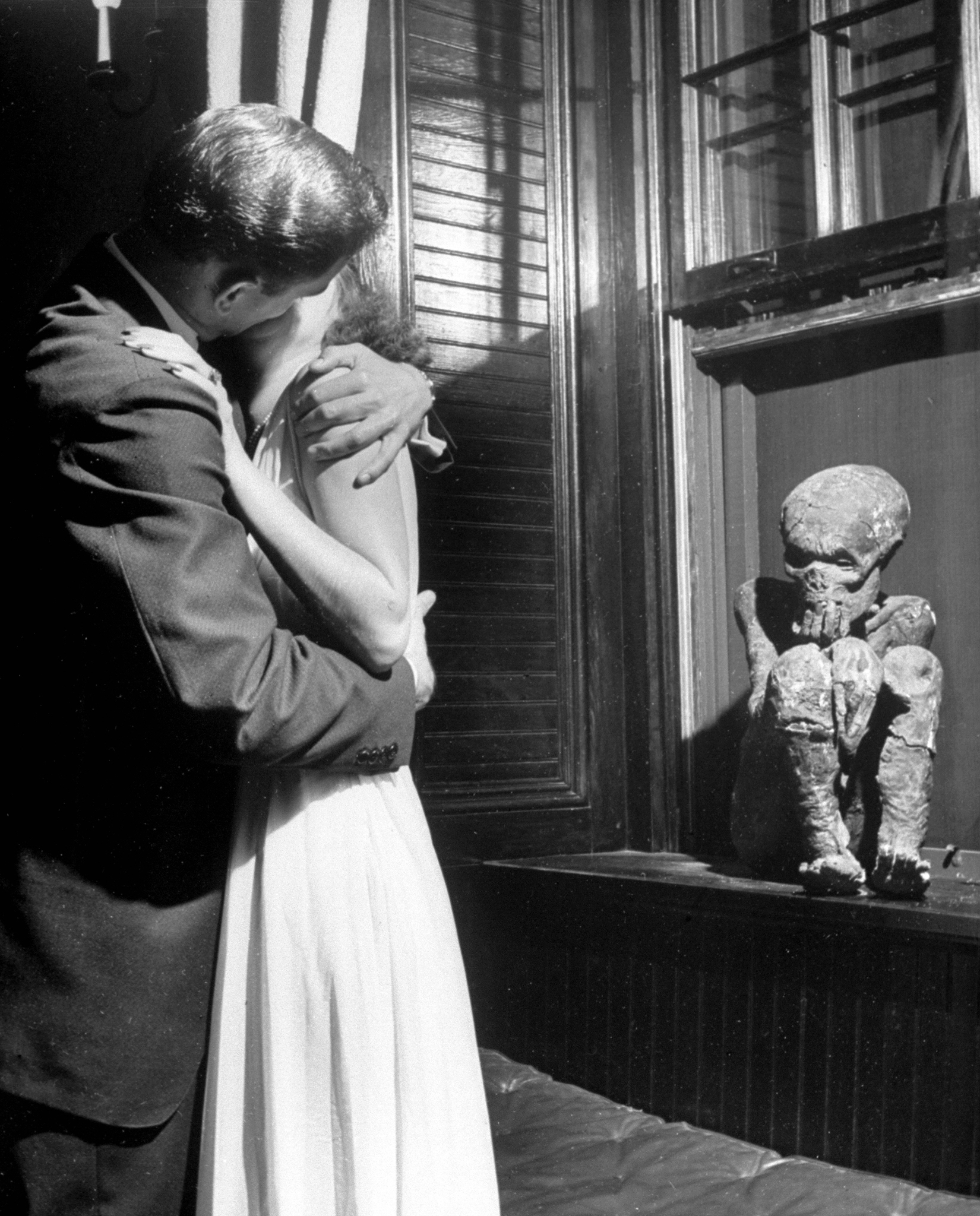 Couple kissing in front of the Delta Tau Delta mummy at the University of the South. Girls are told: "Kiss mummy or kiss me." 1940.