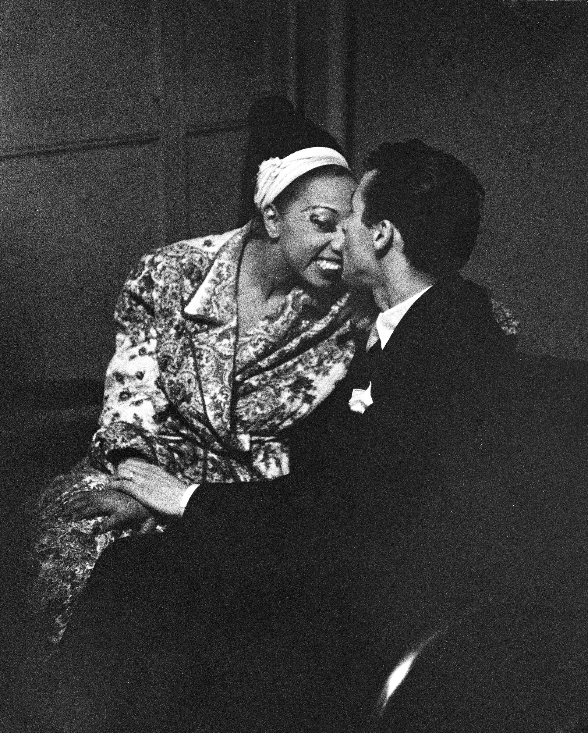 Josephine Baker receiving congratulatory kiss on the nose from her husband, orchestra leader Jo Bouillon, after her show at the Strand theater during her US tour. 1951.