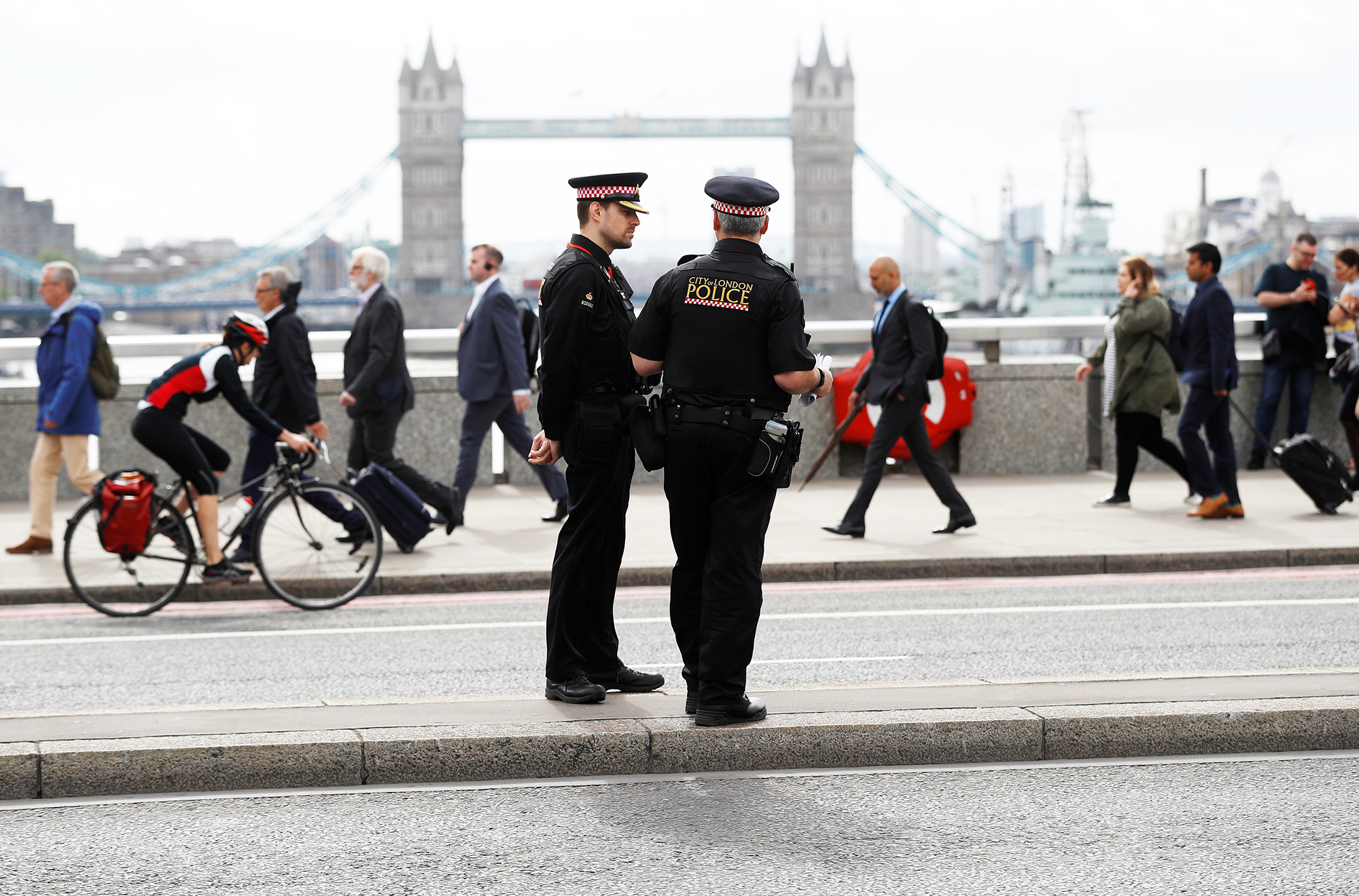 Commuters travel past City of London police officers standing on London Bridge after is was reopened following an attack which left 7 people dead and dozens of injured in central London