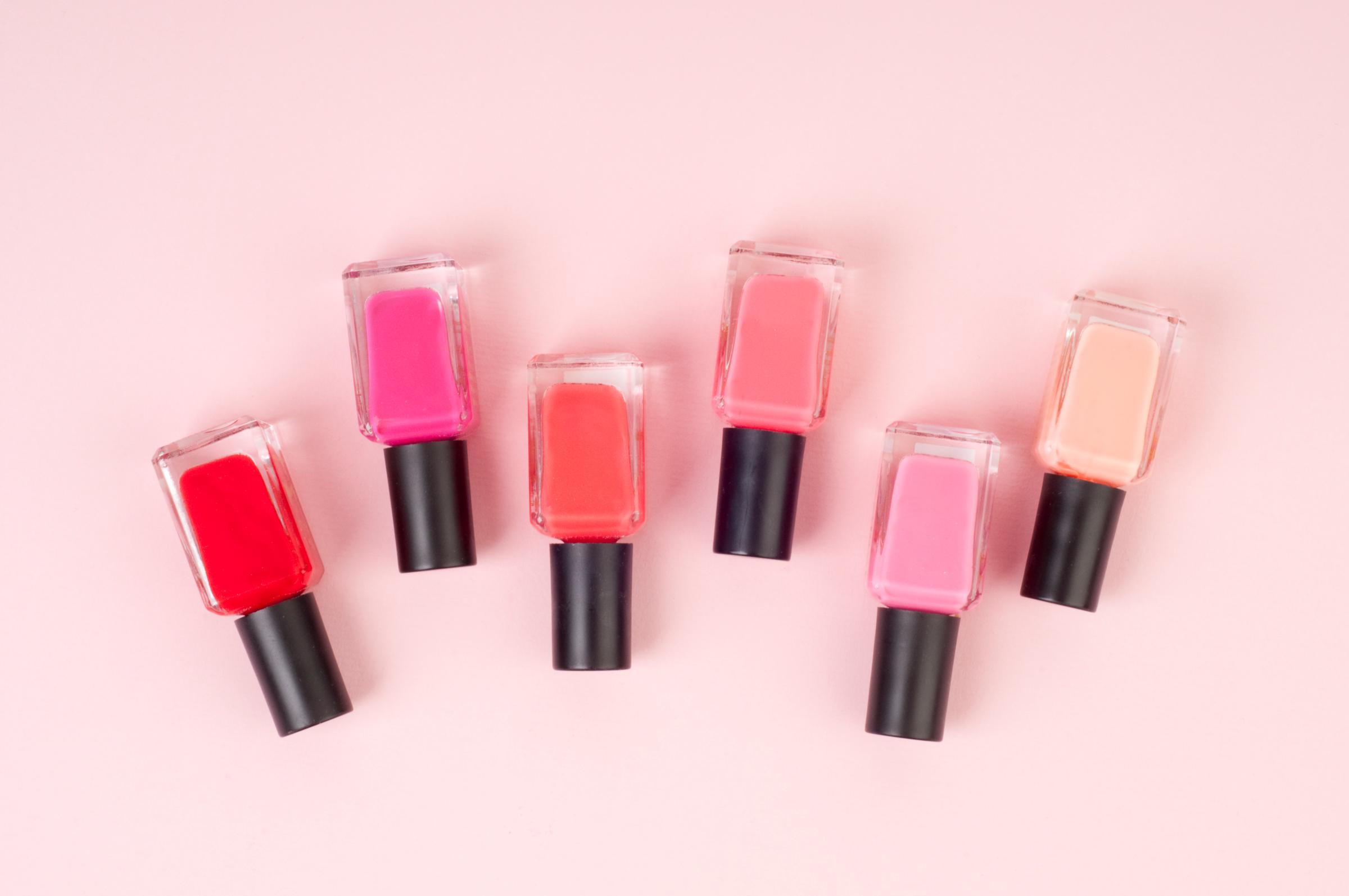 Row of six small bottles of nail polish in various shades of pink, overhead view