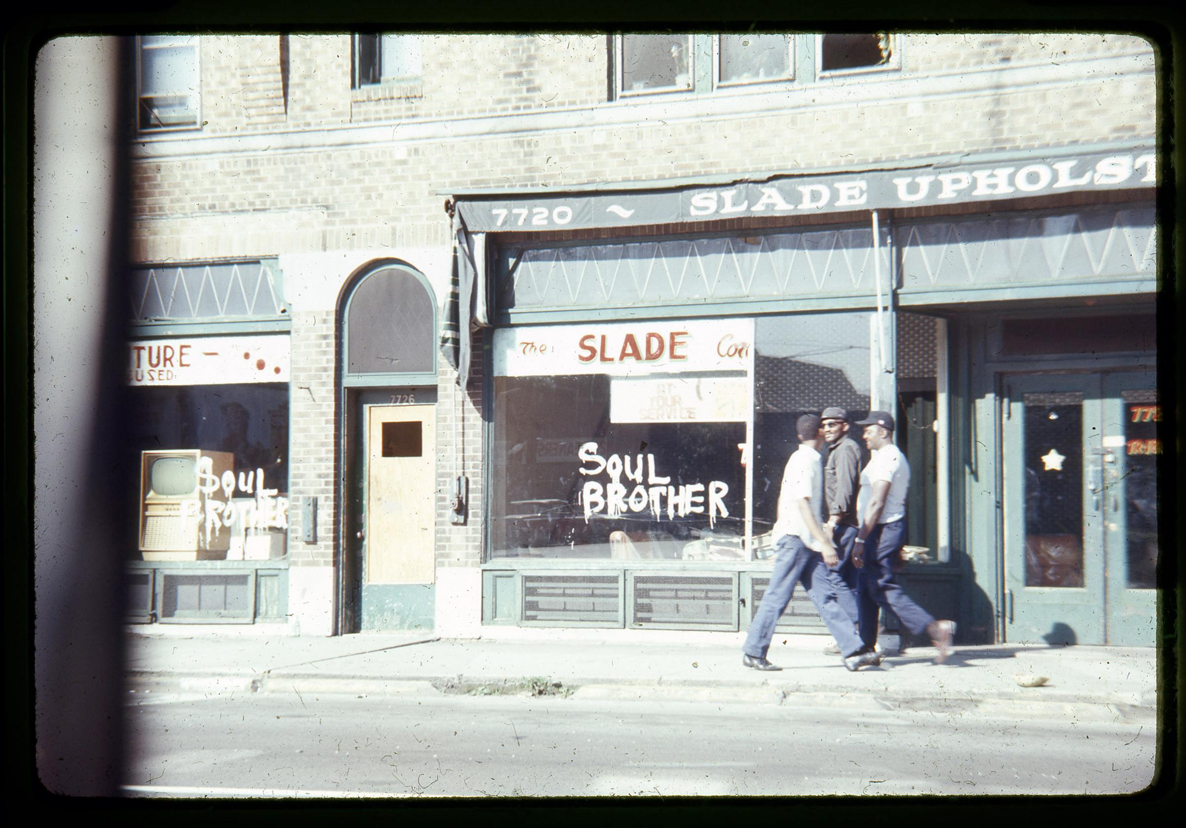 Citizens walk past a store spray painted with the phrase “Soul Brother,” signifying the store is African American owned in an attempt to prevent vandalism and looting.