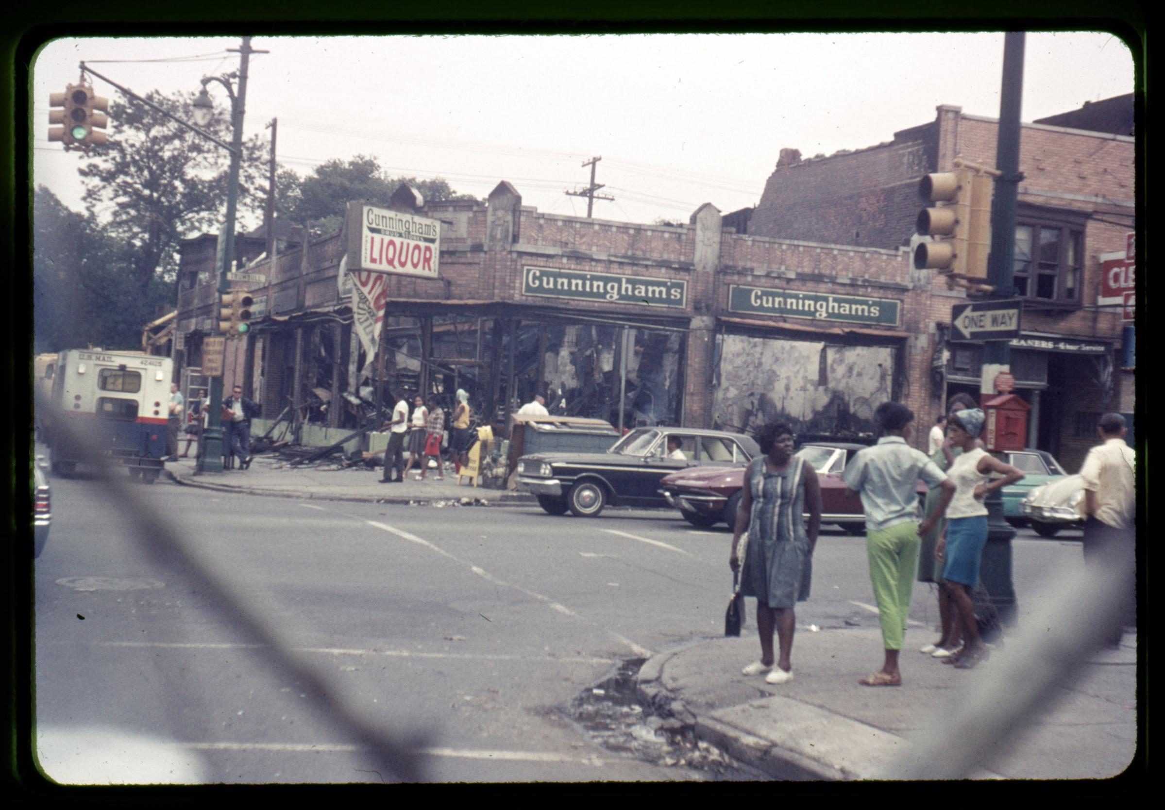 Pedestrians and bystanders observe the devastated buildings on the corner of Trumbull and Forest Avenue in Detroit, July 1967.