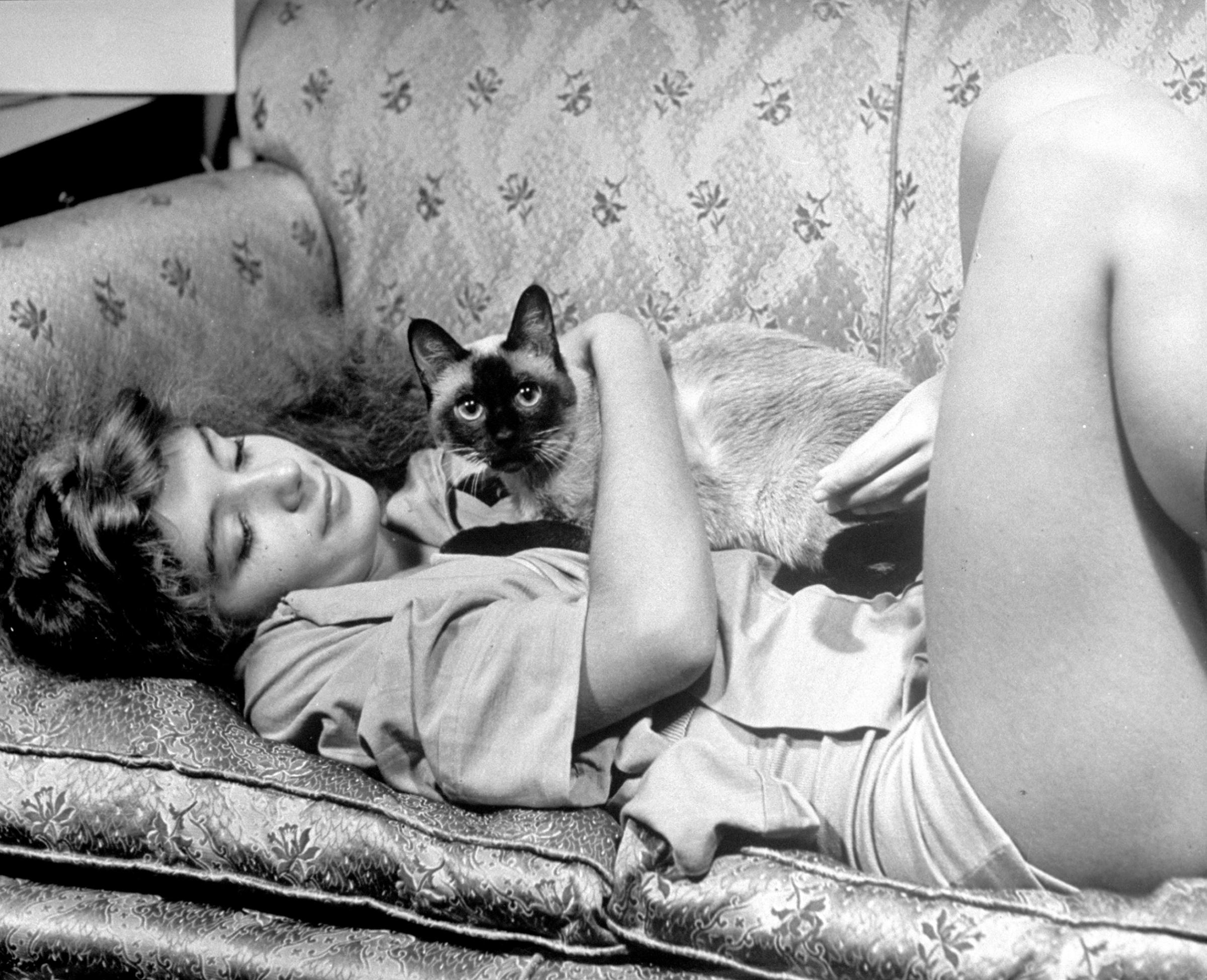 Aspiring ballerina Edwina Seaver relaxing on sofa at home with Siamese cat Ting Ling, 1940.