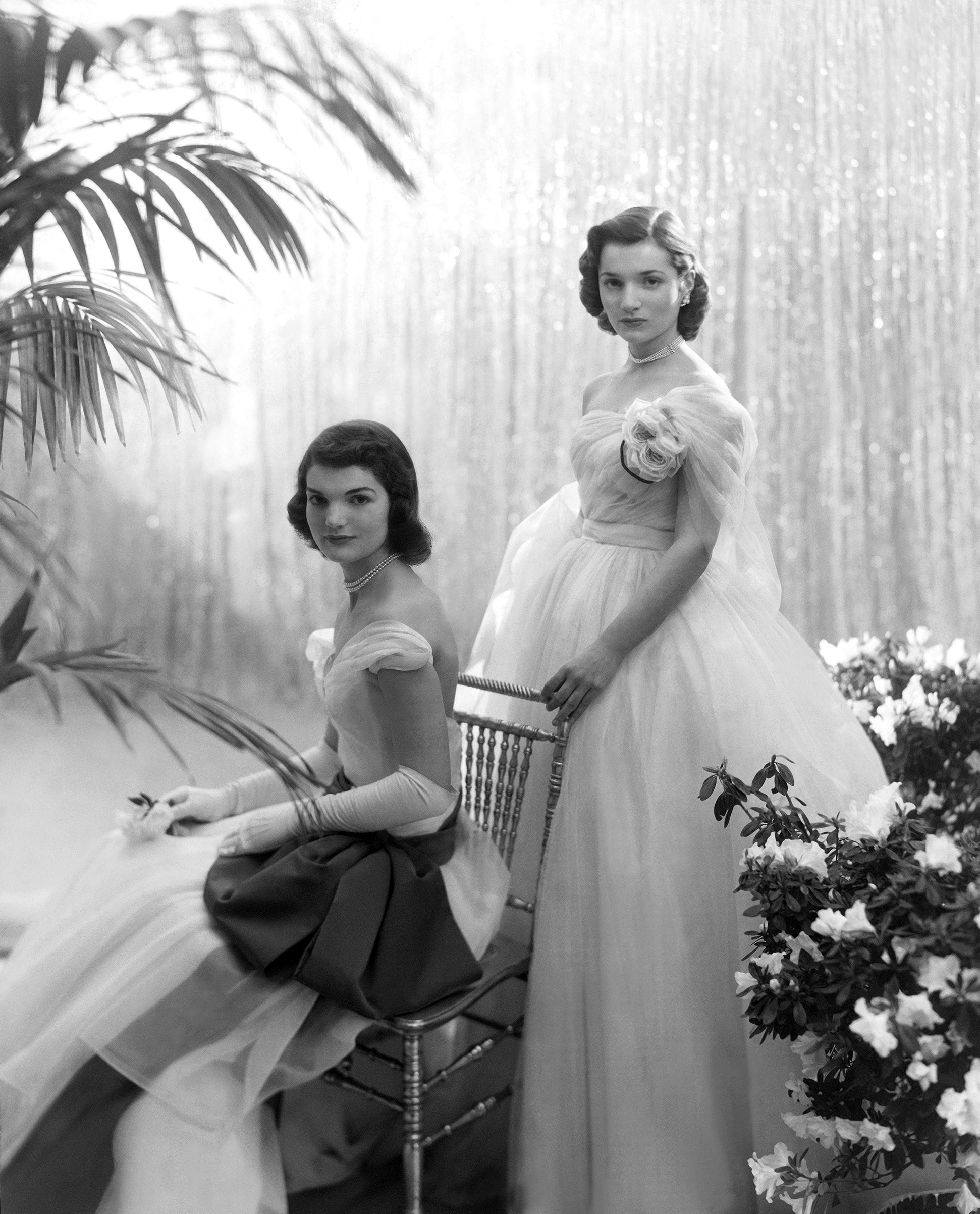 Jacqueline Bouvier (later Jacqueline Kennedy Onassis), seated, with her sister Caroline Lee Bouvier, standing behind her, wearing ball gowns, 1951.