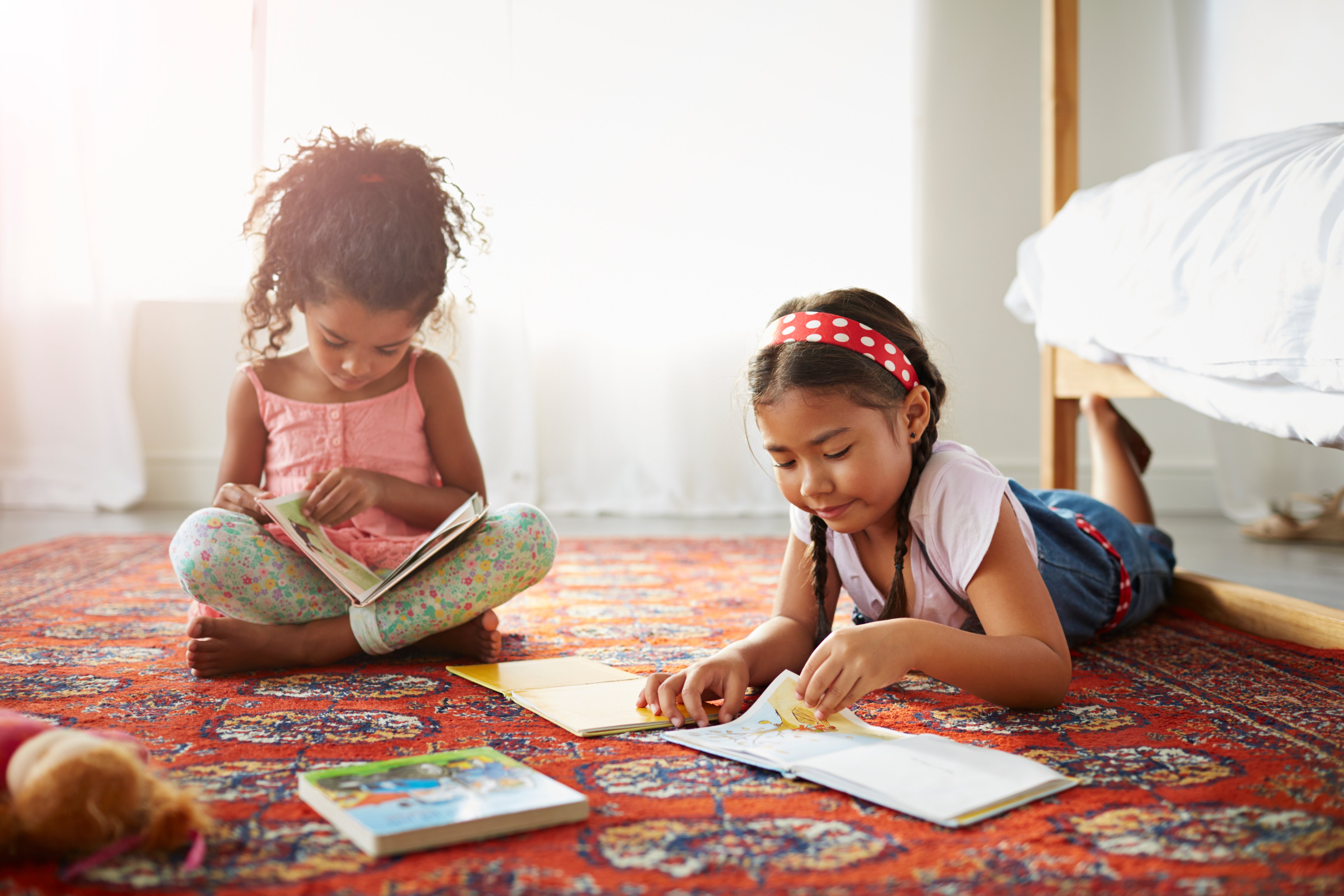 Two sisters reading books on the floor in bedroom
